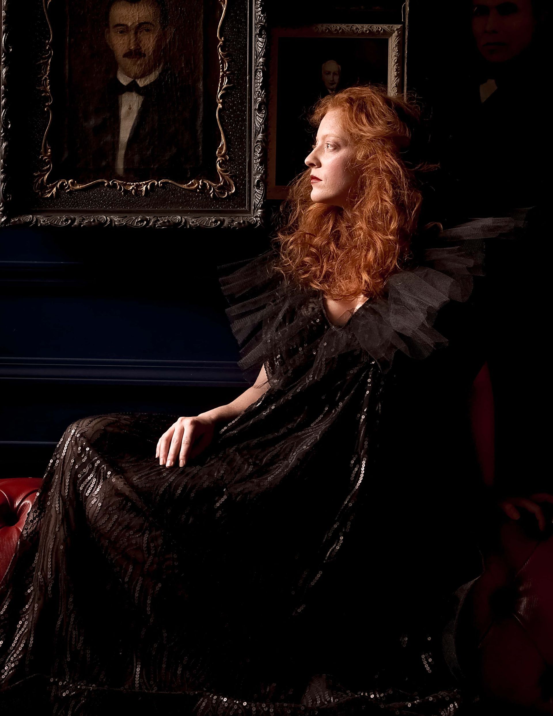 A woman in a black dress is sitting in front of a painting of a man