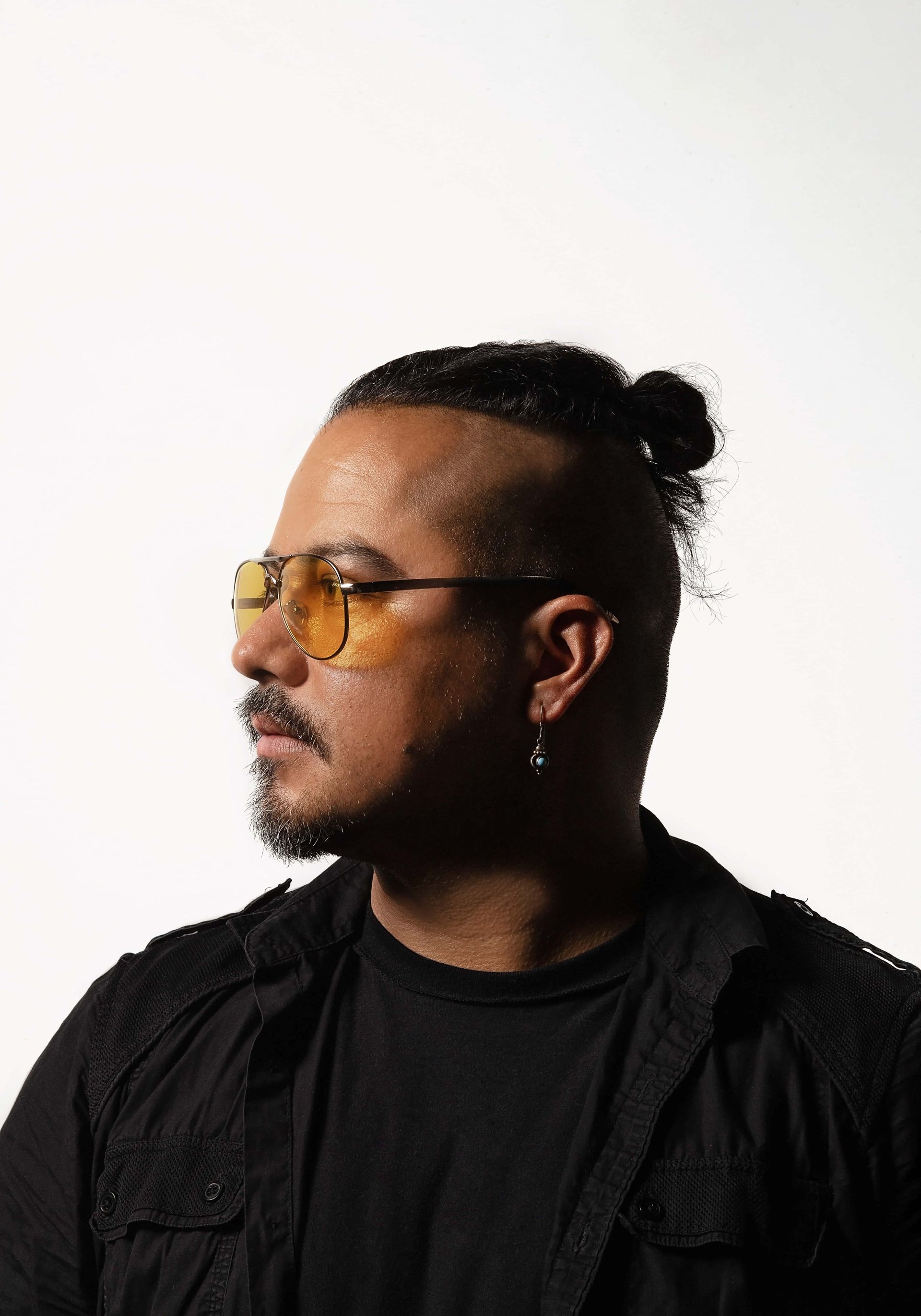 A man wearing sunglasses and a bun is looking to the side.