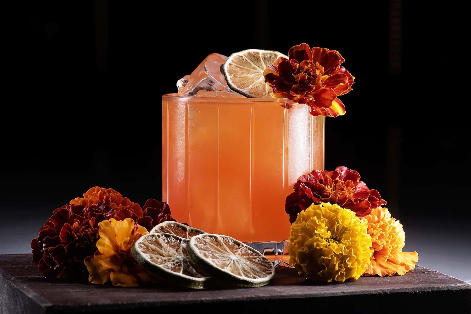 A close up of a drink with flowers and limes on a table.