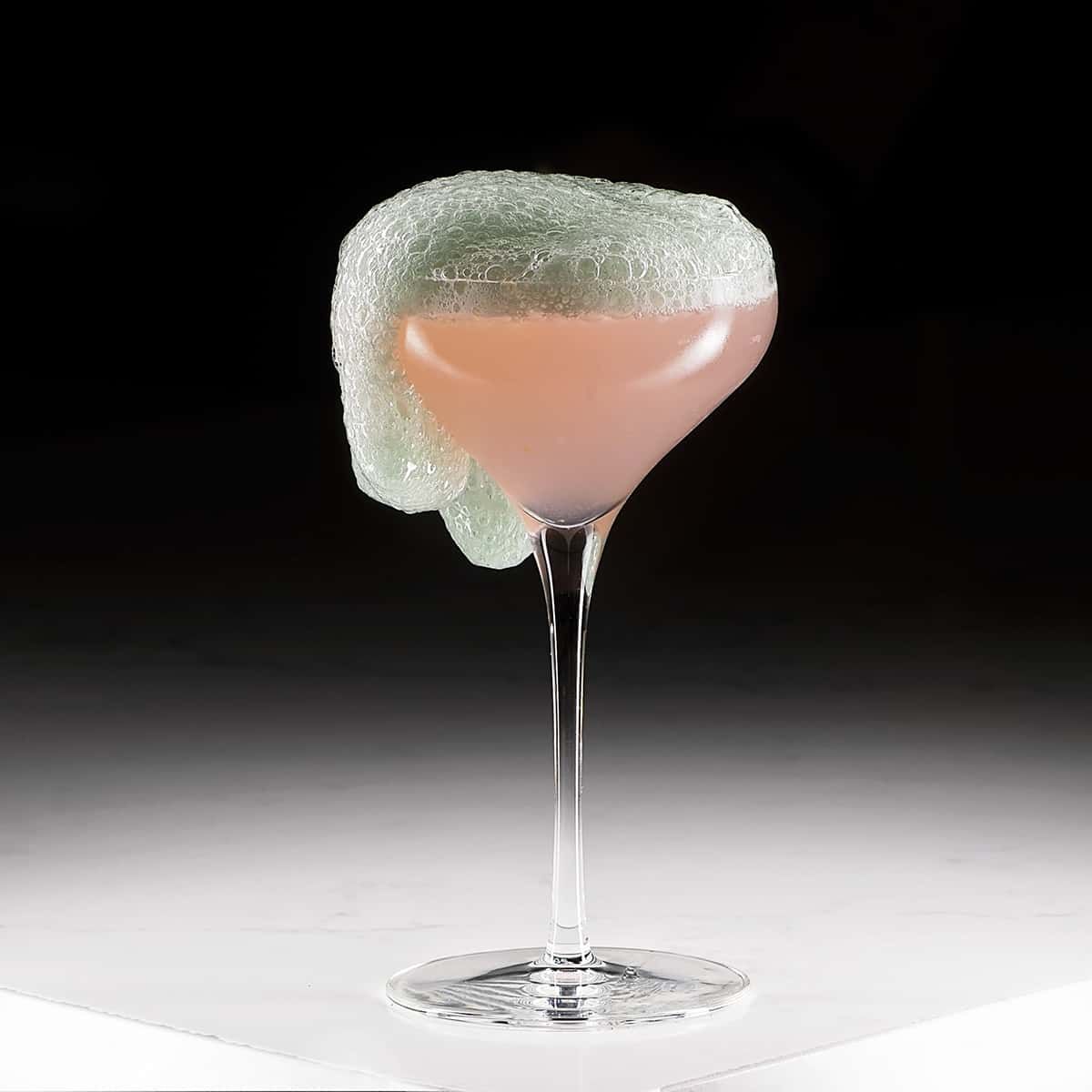 A close up of a cocktail in a wine glass on a table.