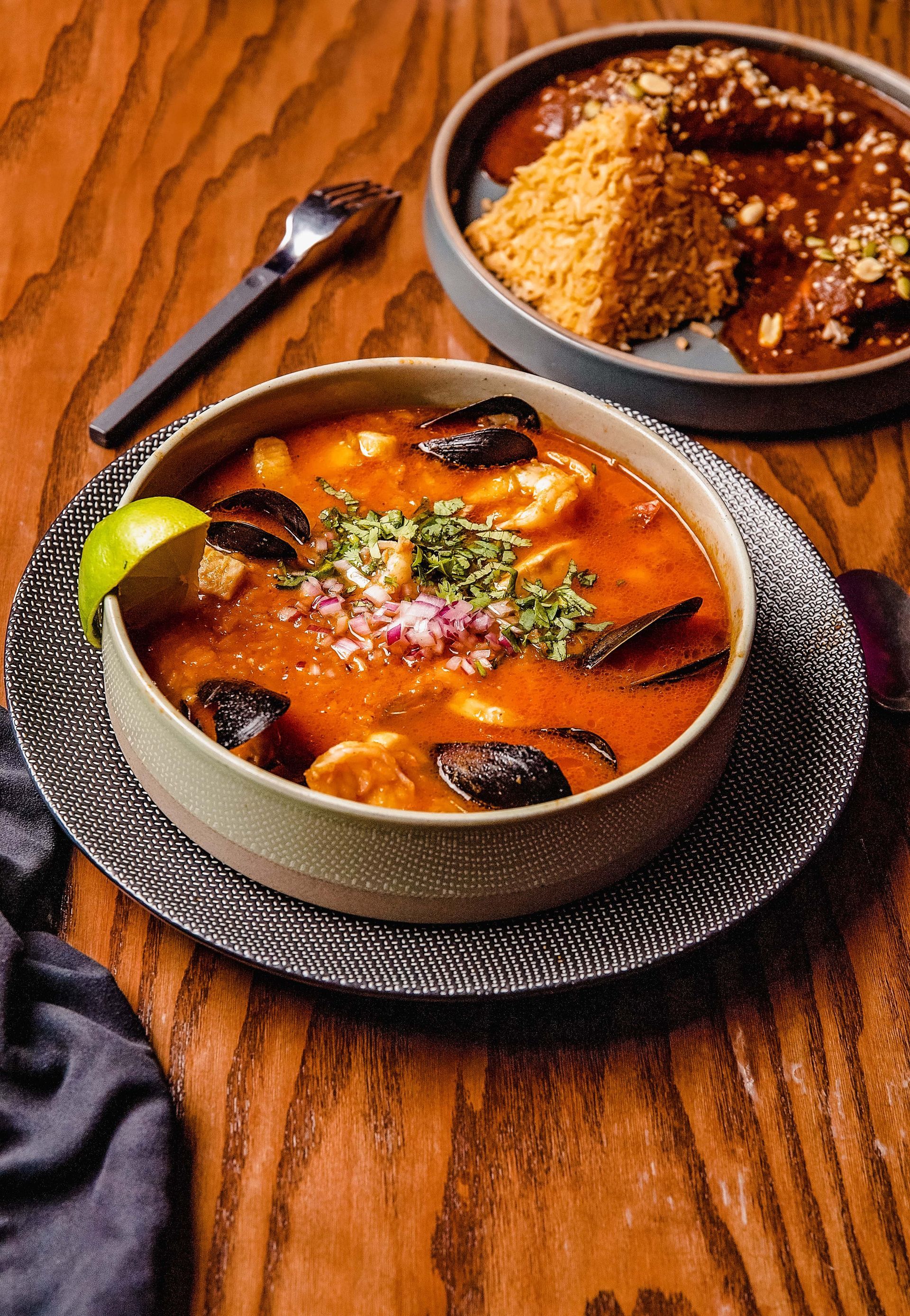 A bowl of soup and a plate of food on a wooden table.