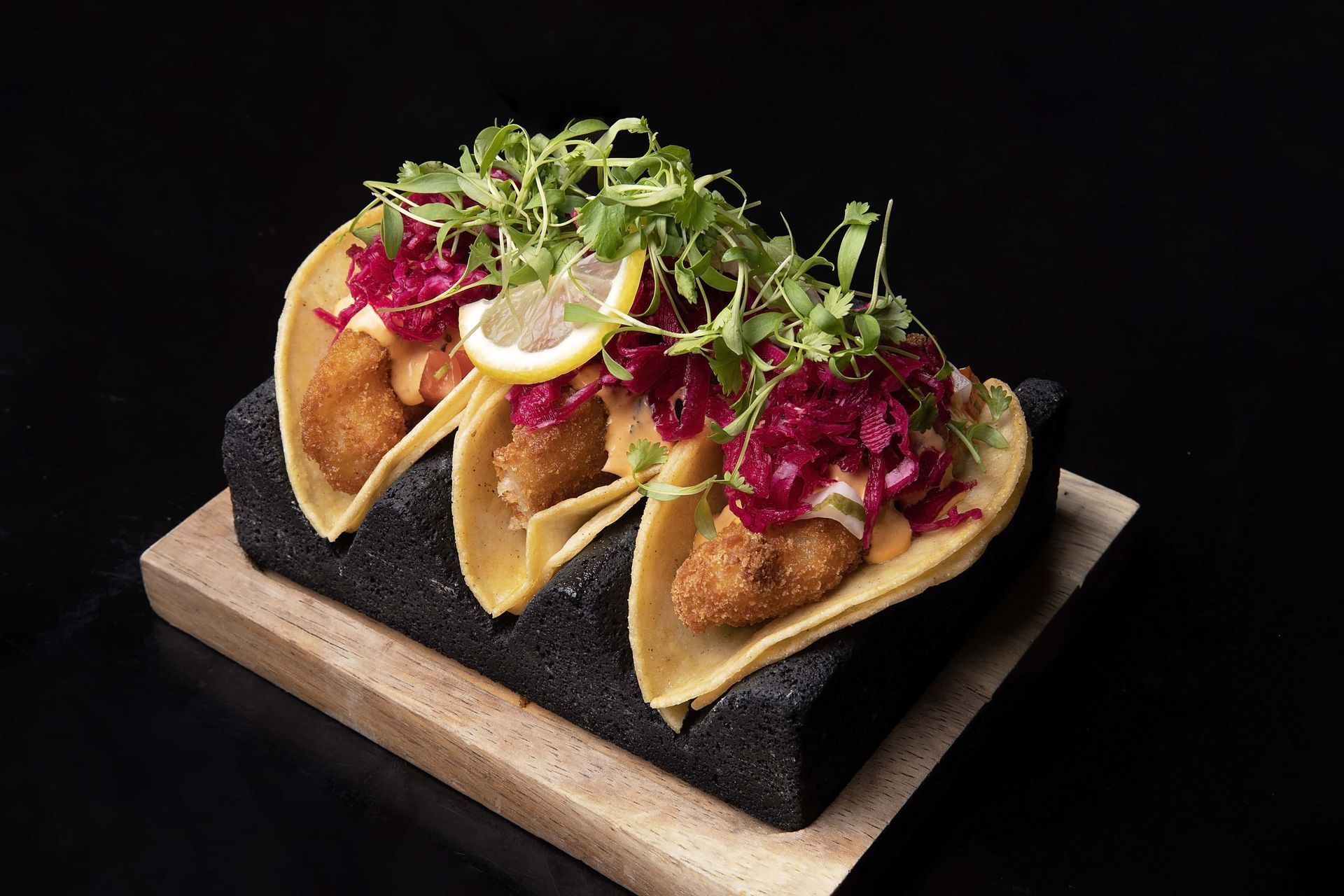Three tacos are sitting on top of a wooden cutting board.
