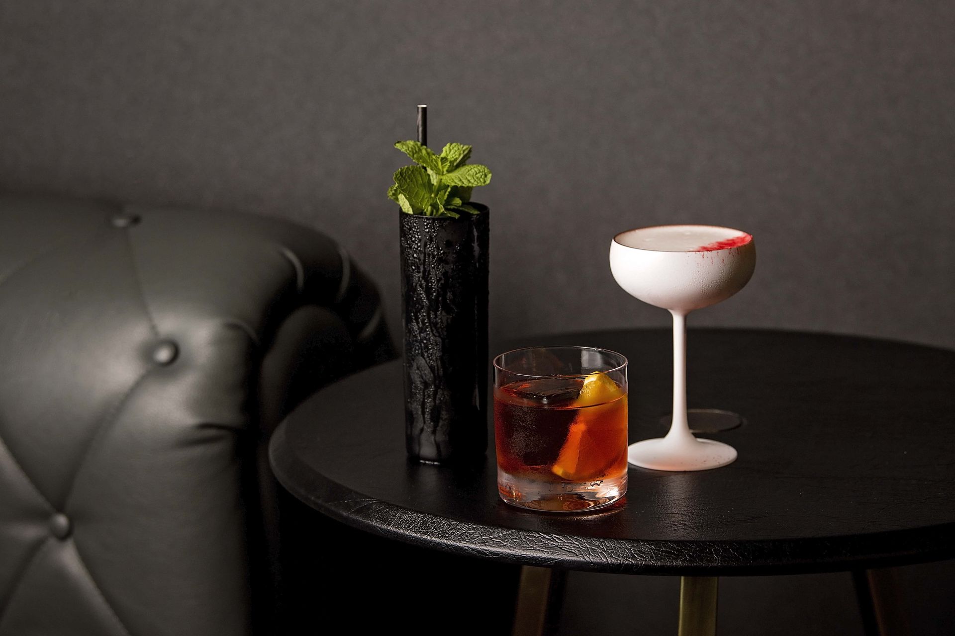Two drinks are on a table next to a black couch.