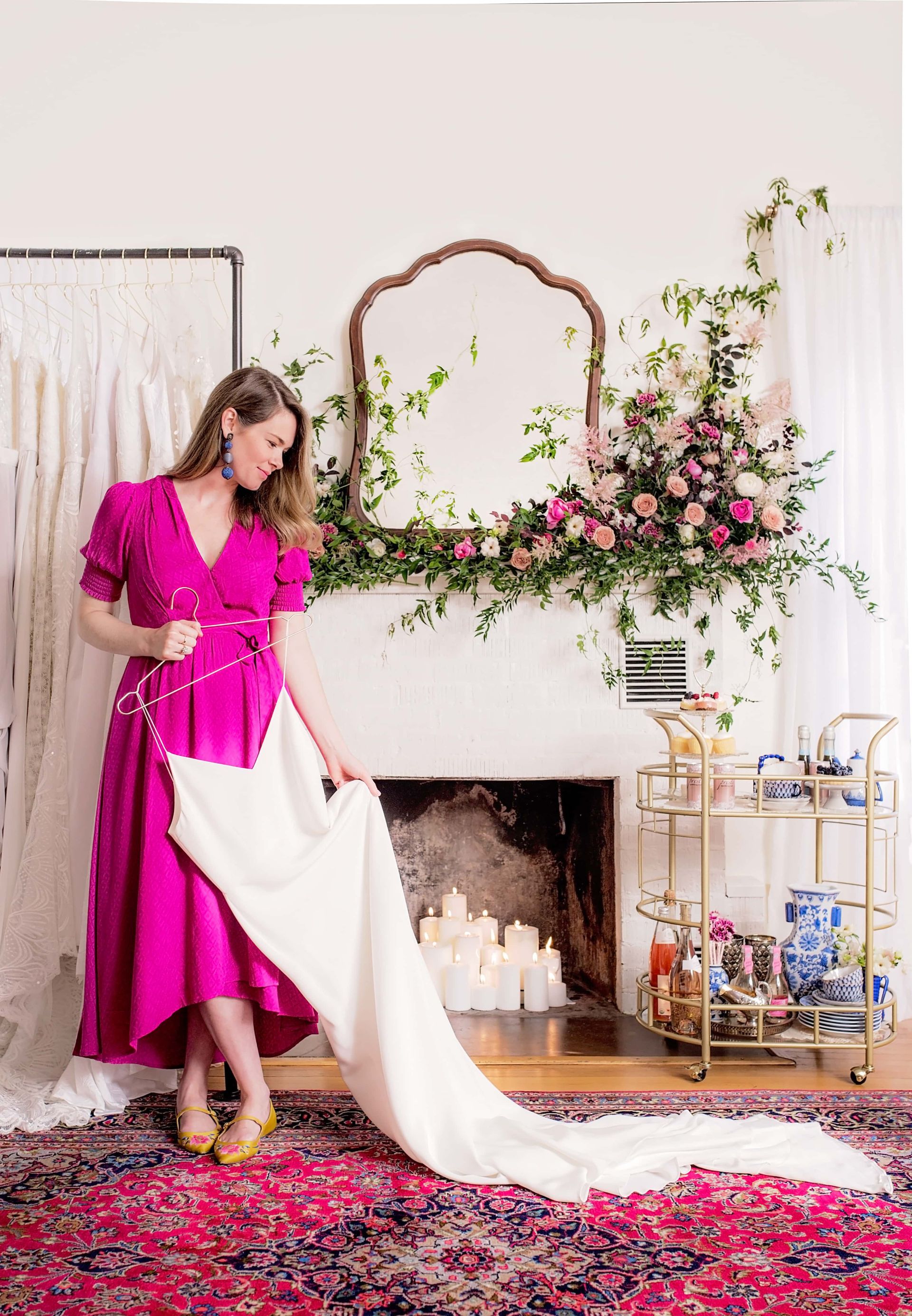 A woman in a pink dress is standing in front of a fireplace holding a white cloth.