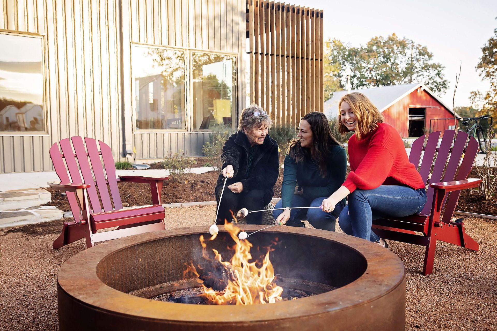 Three people are sitting around a fire pit roasting marshmallows.