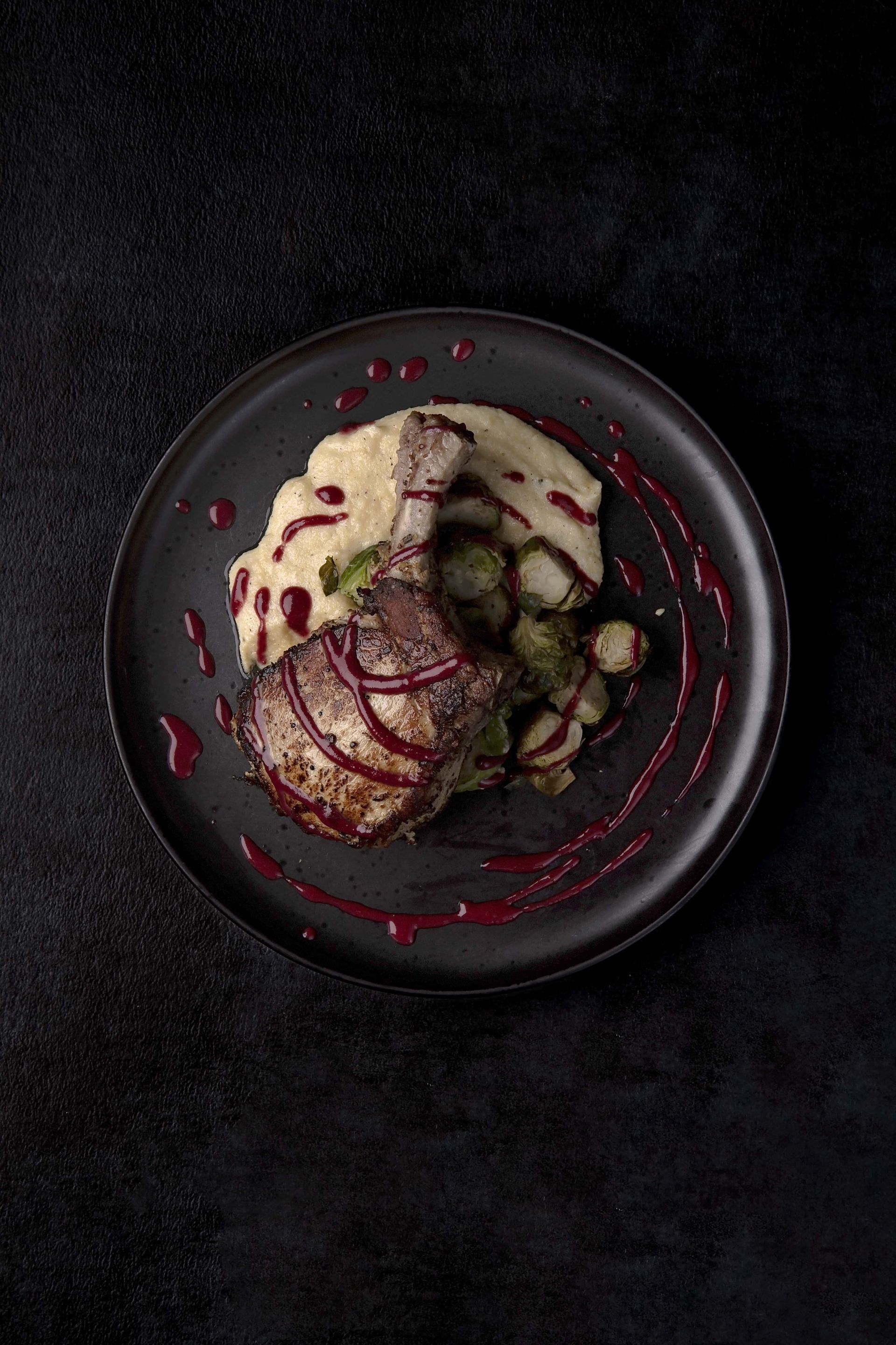 A black plate topped with meat and mashed potatoes on a black table.