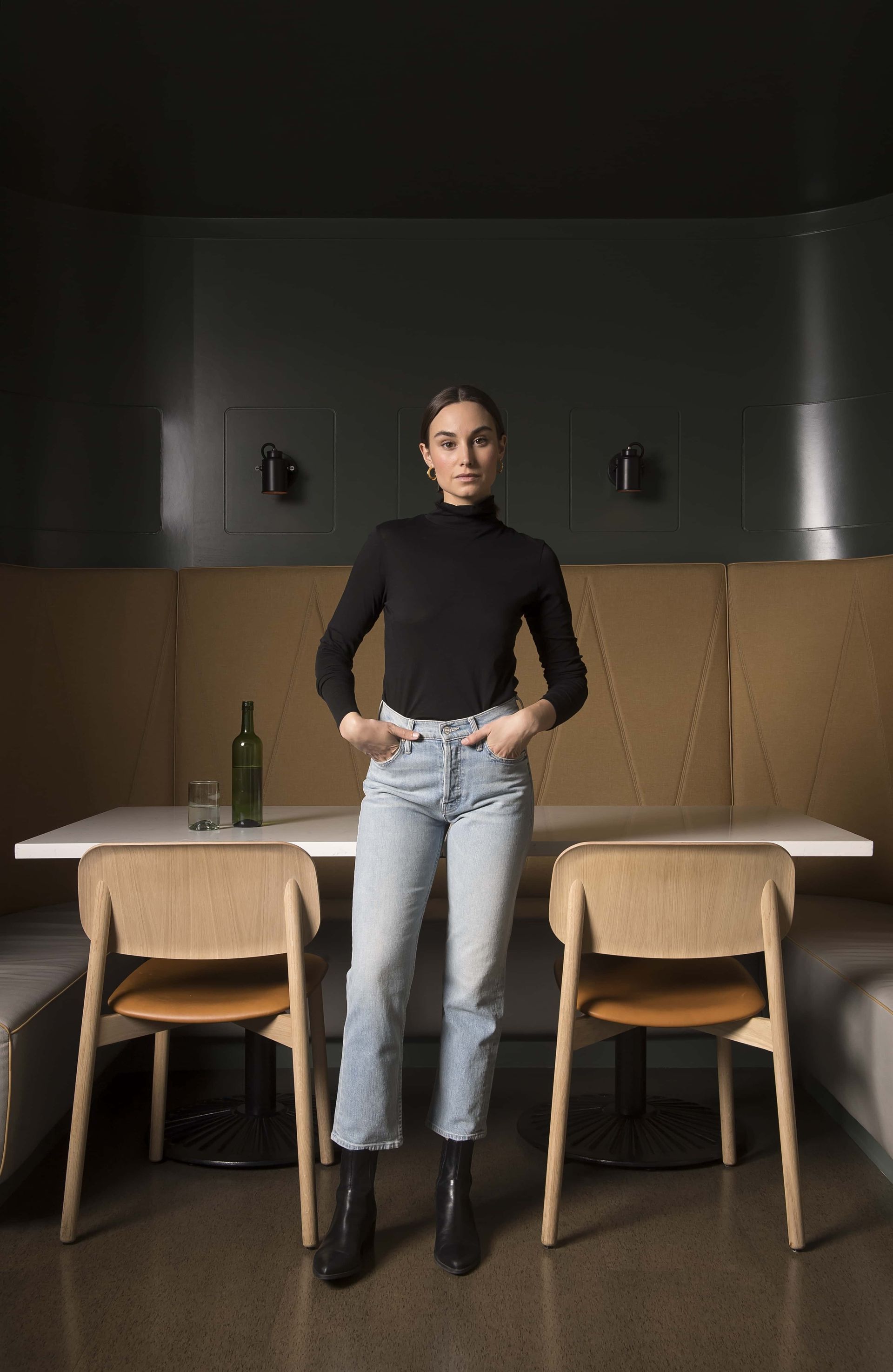 A woman is standing in front of a table and chairs in a restaurant.