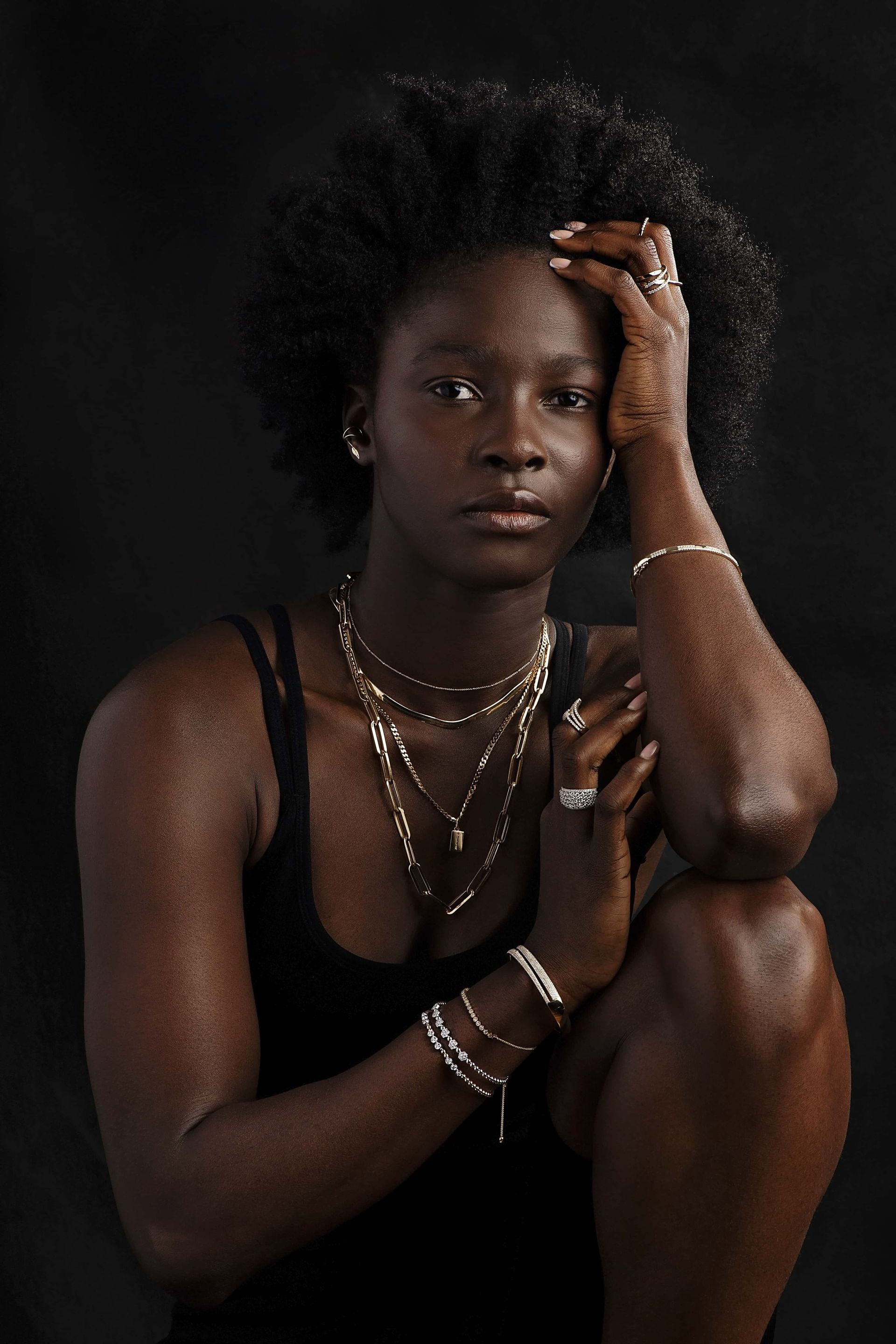 A woman wearing a black tank top , necklaces , bracelets and rings is kneeling down.