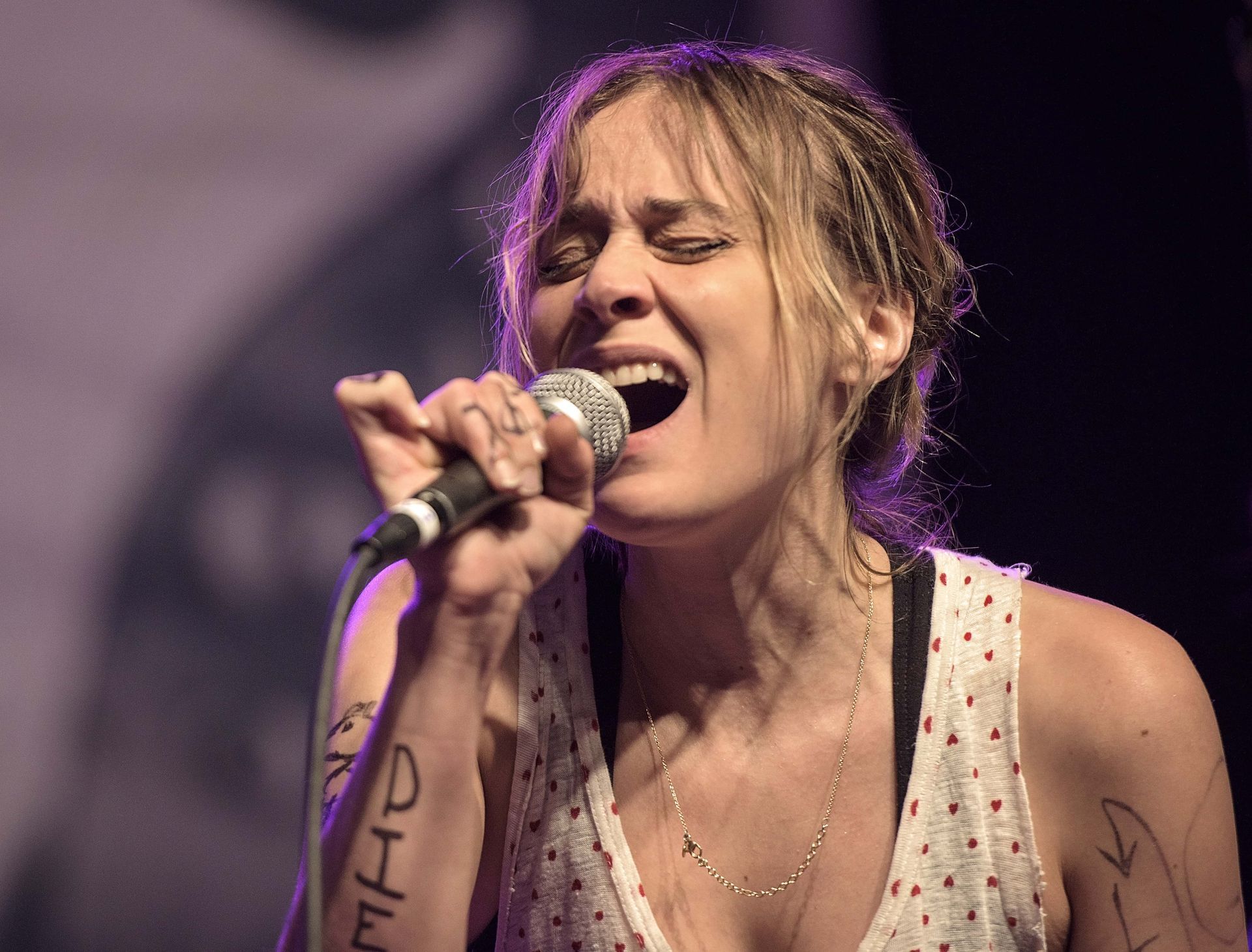 A woman singing into a microphone with graffiti on her arm