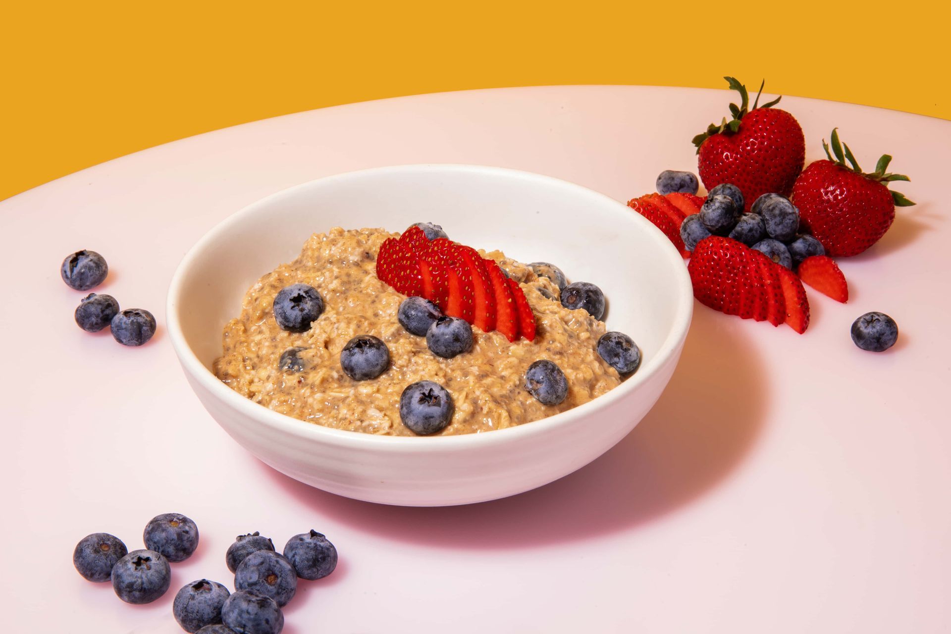 A bowl of oatmeal with blueberries and strawberries on a table.