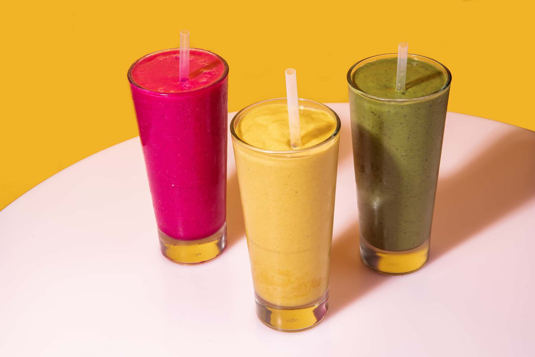 Three smoothies with straws are sitting on a white table.