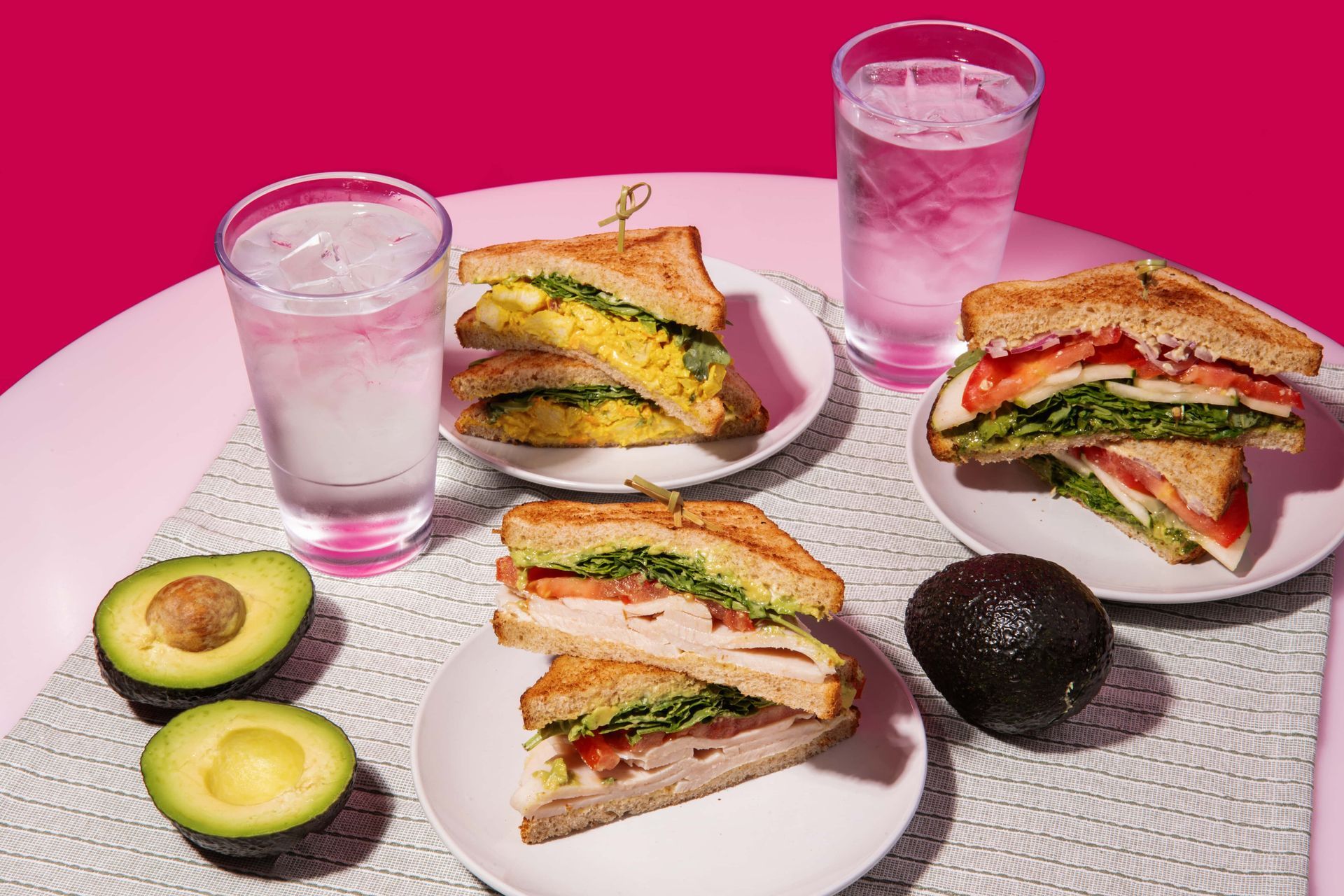 A table topped with plates of sandwiches , avocados , and water.