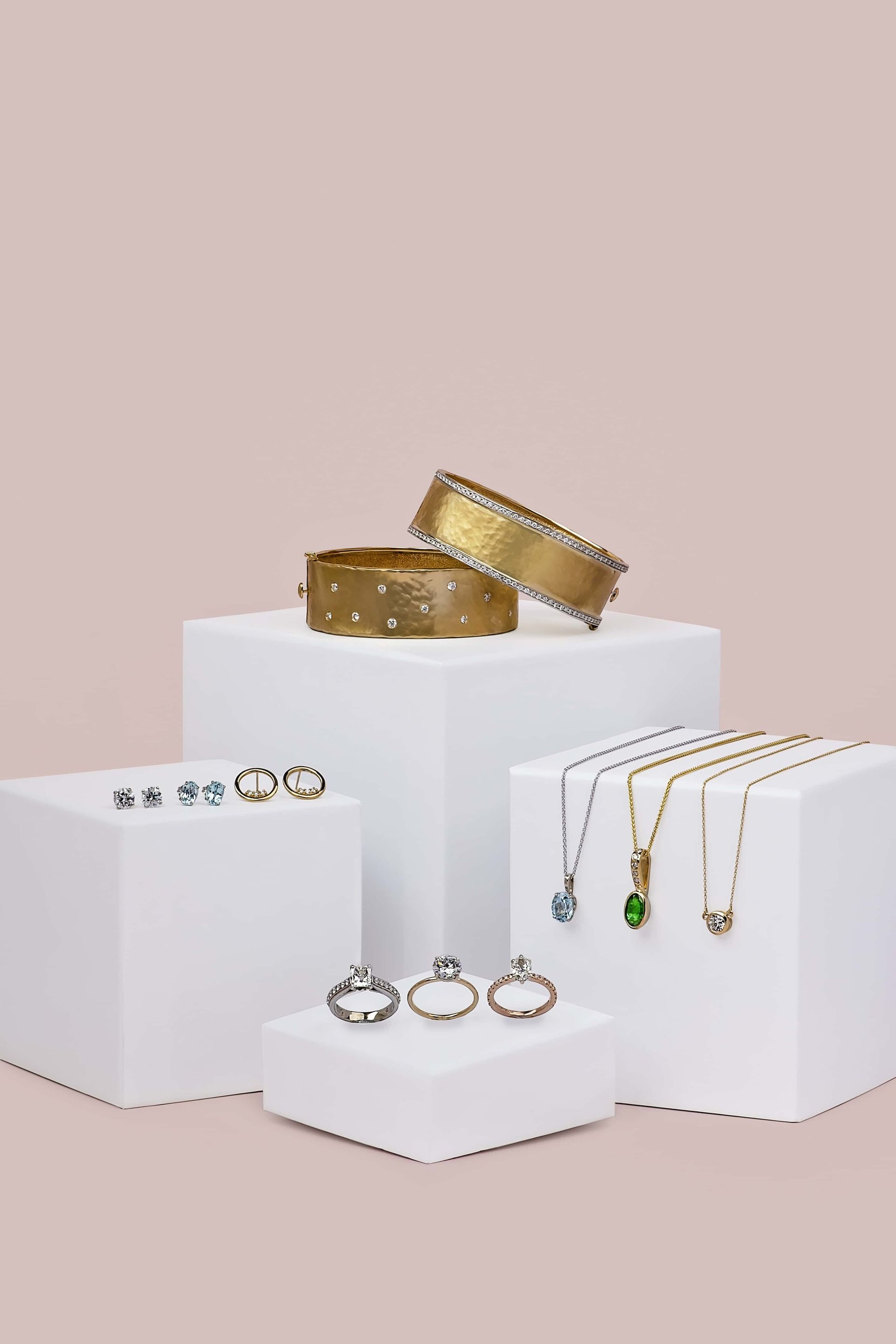 A group of jewelry displayed on white blocks on a pink background.