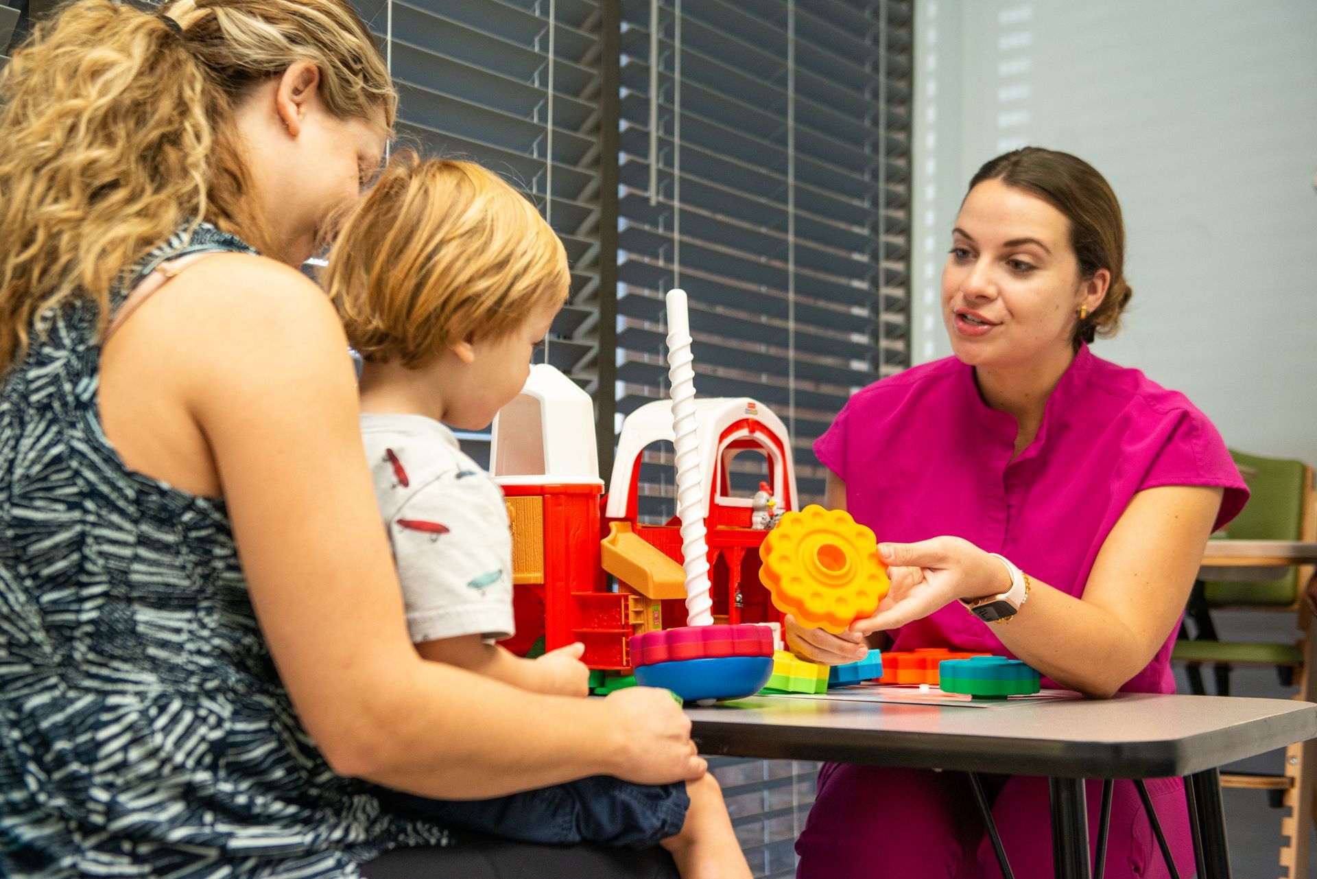 Therapist showing a toy to a child and parent in a clinical setting.