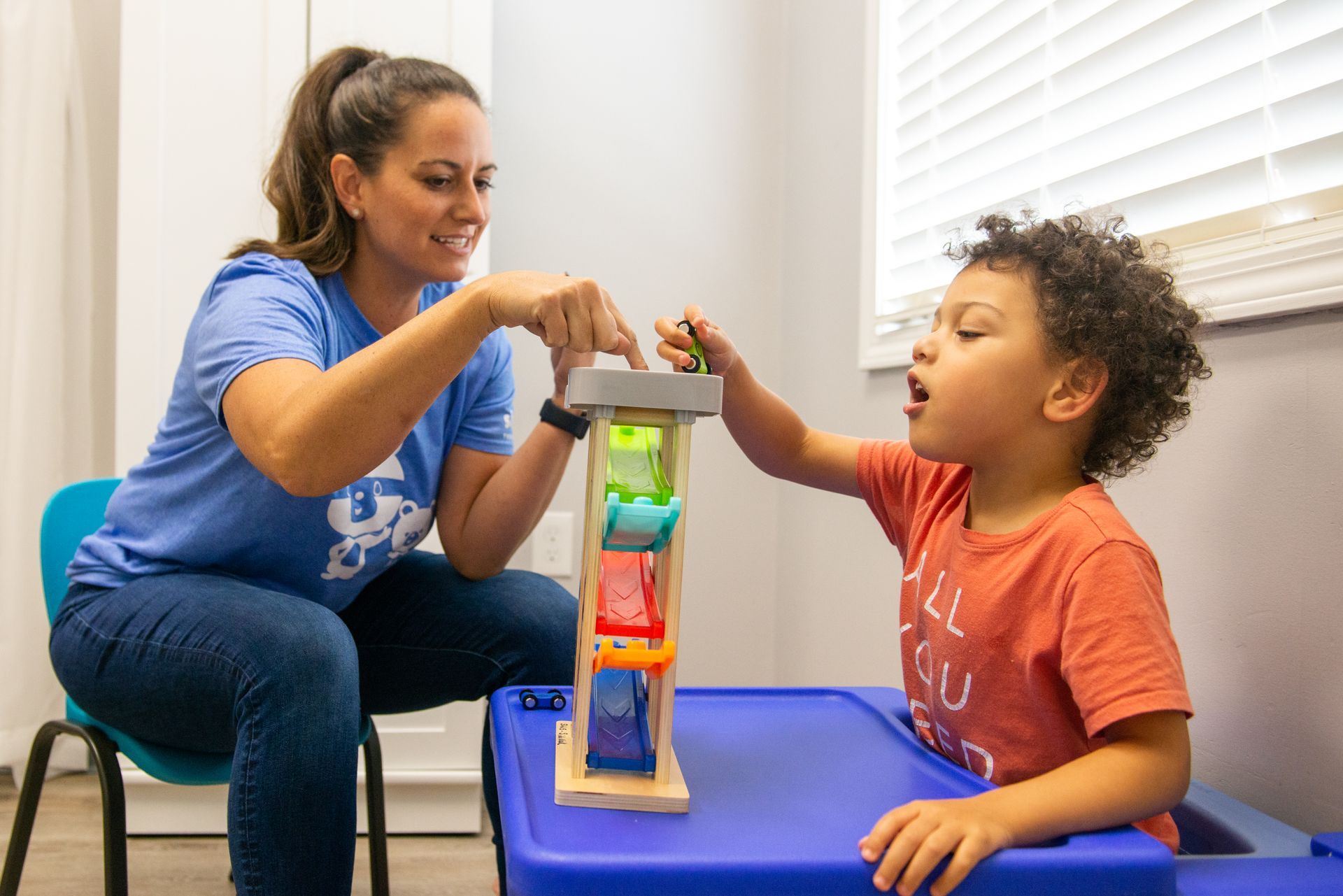 Woman and child playing with a car ramp toy, indoors. The woman is guiding the cars.