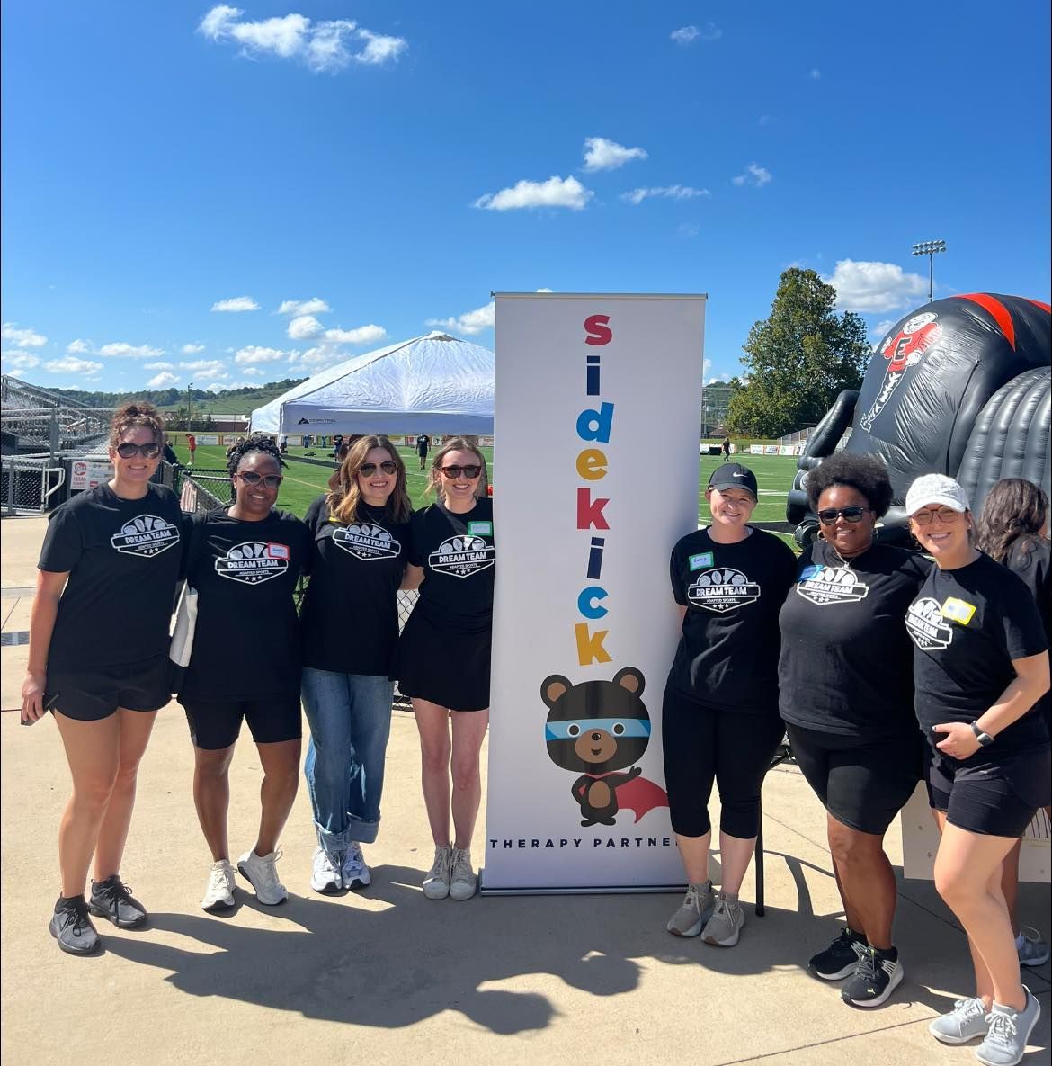 Group of people in black shirts pose by a banner with