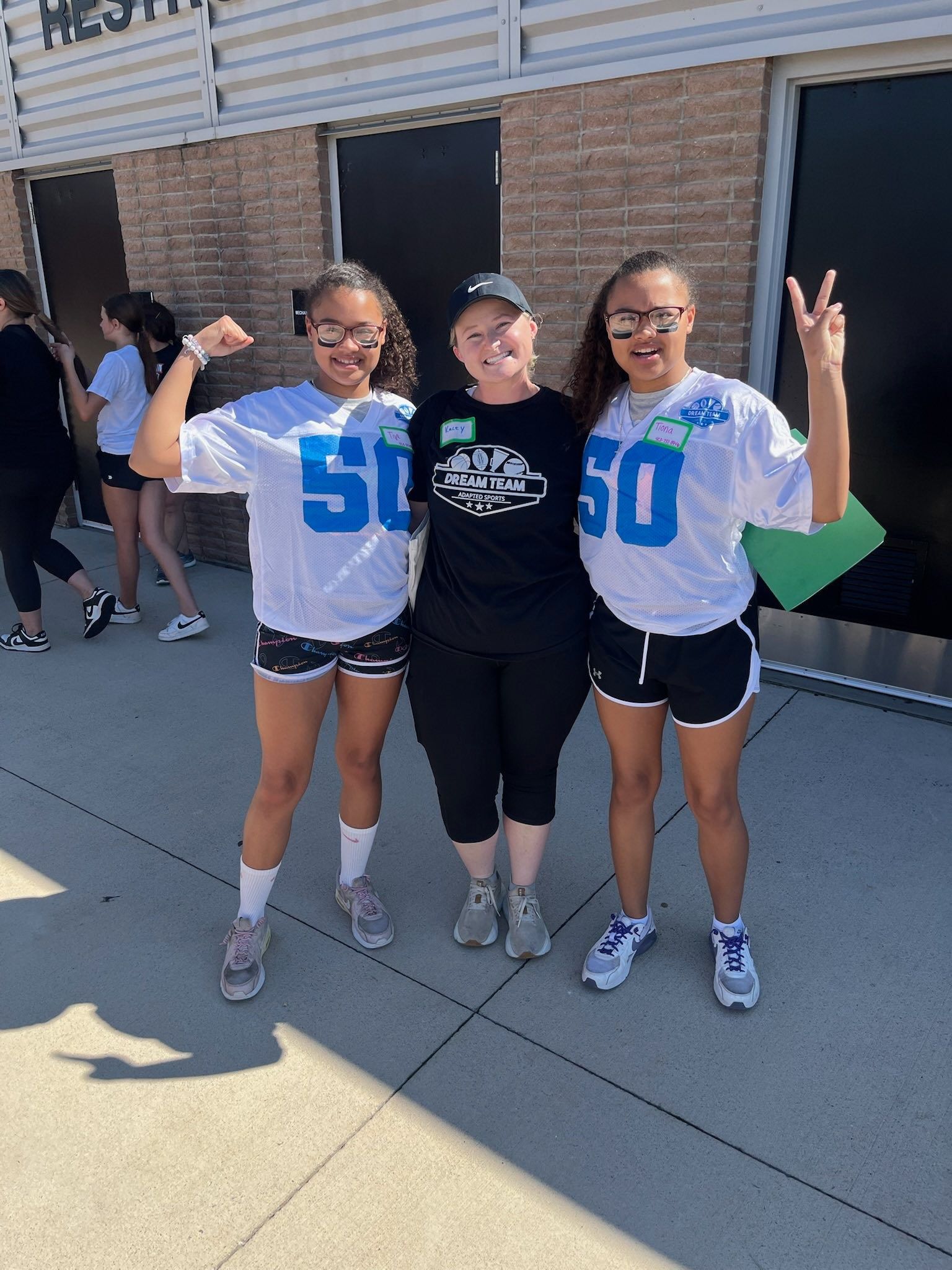 Three people posing outdoors. Two girls in matching white shirts with
