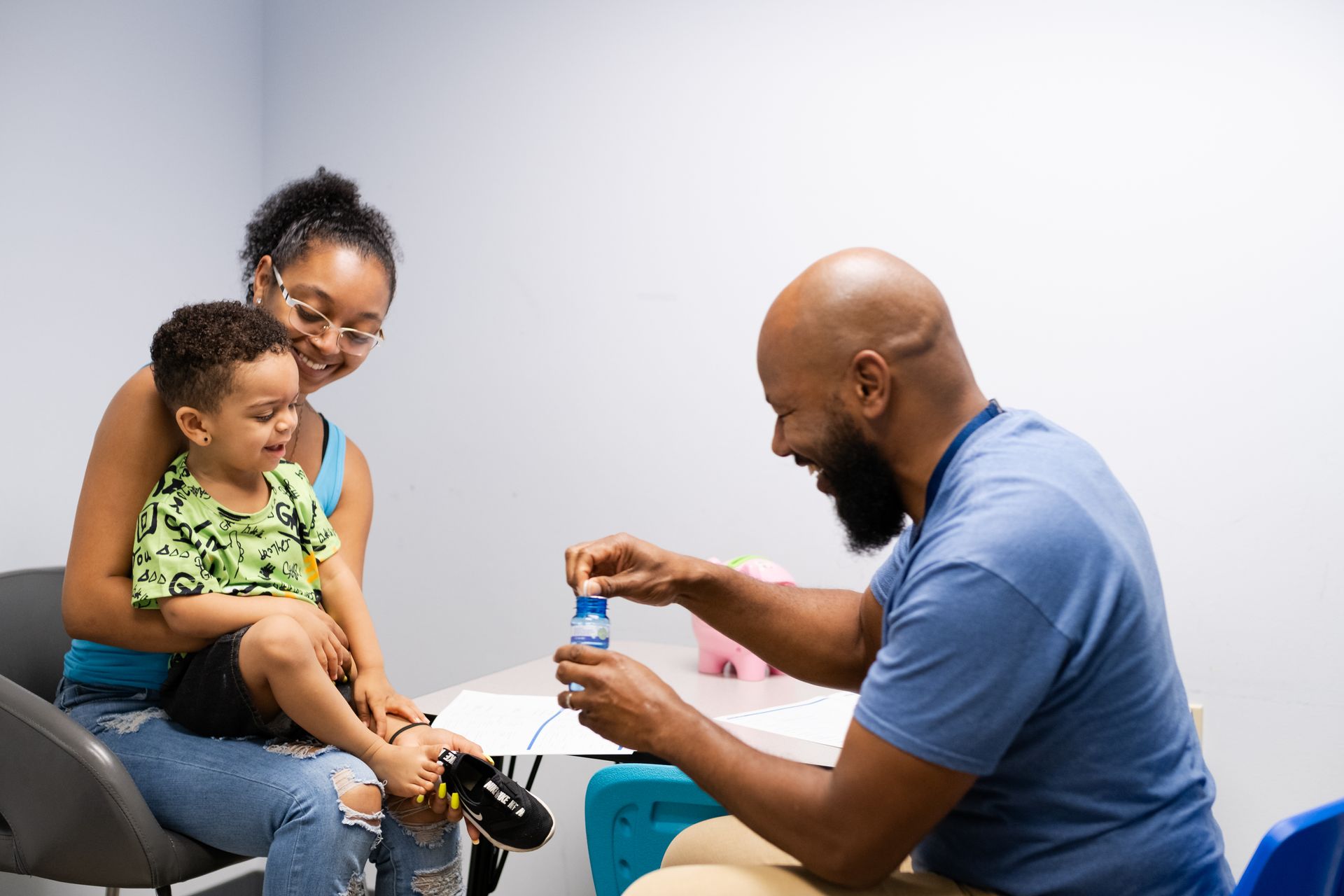 A person blowing bubbles for a child and adult in a room with a table.