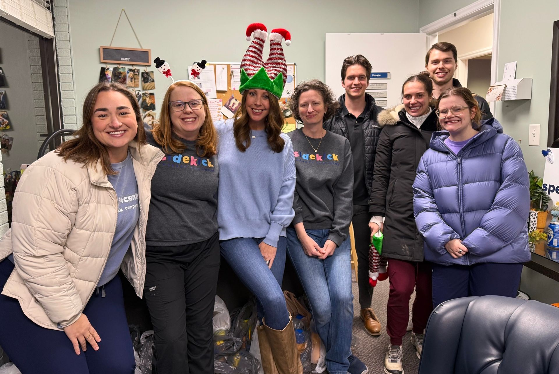 Group of people smiling, indoors. Some wear matching shirts. One person has elf hat.