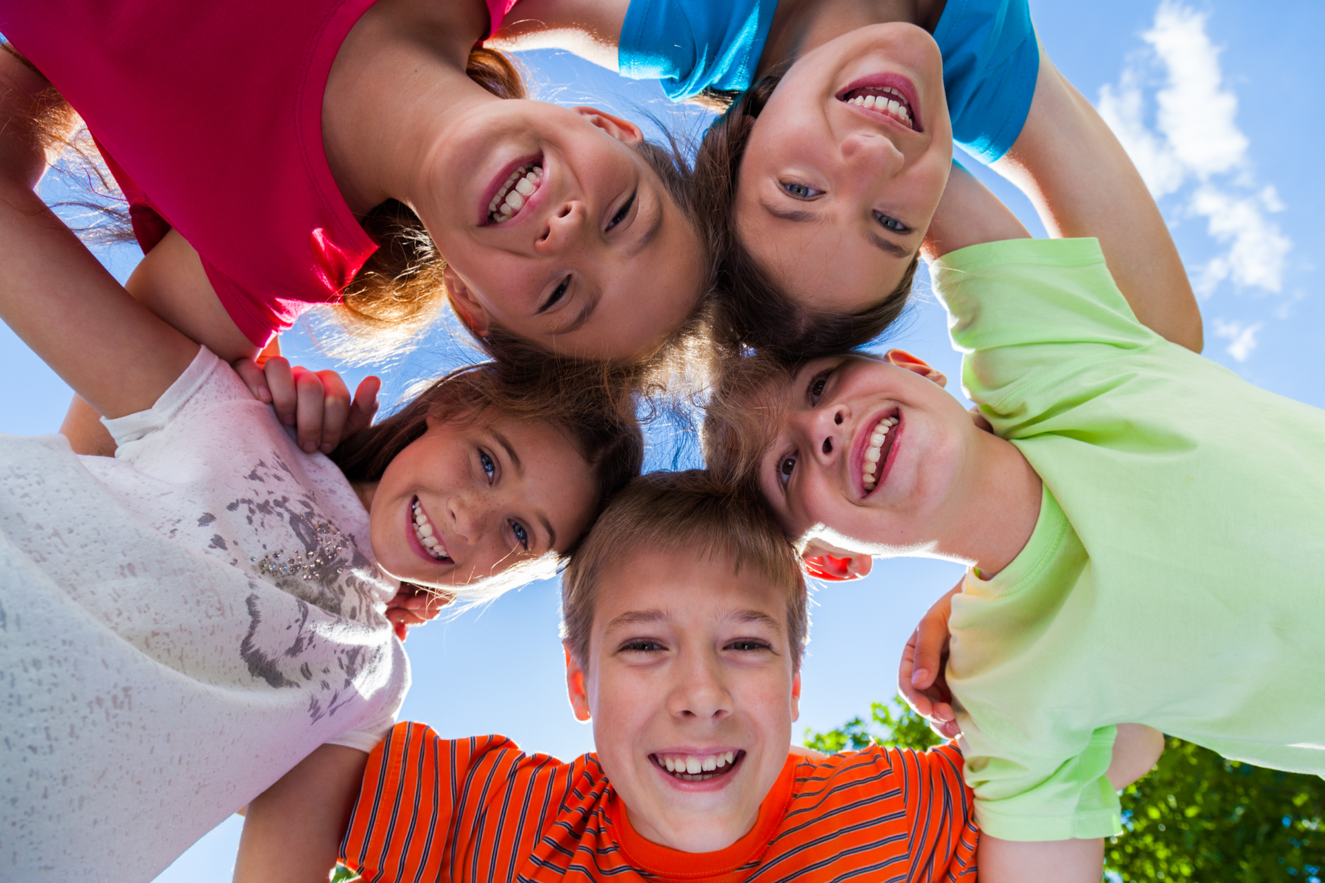 Five smiling children huddle together, forming a circle against a blue sky.