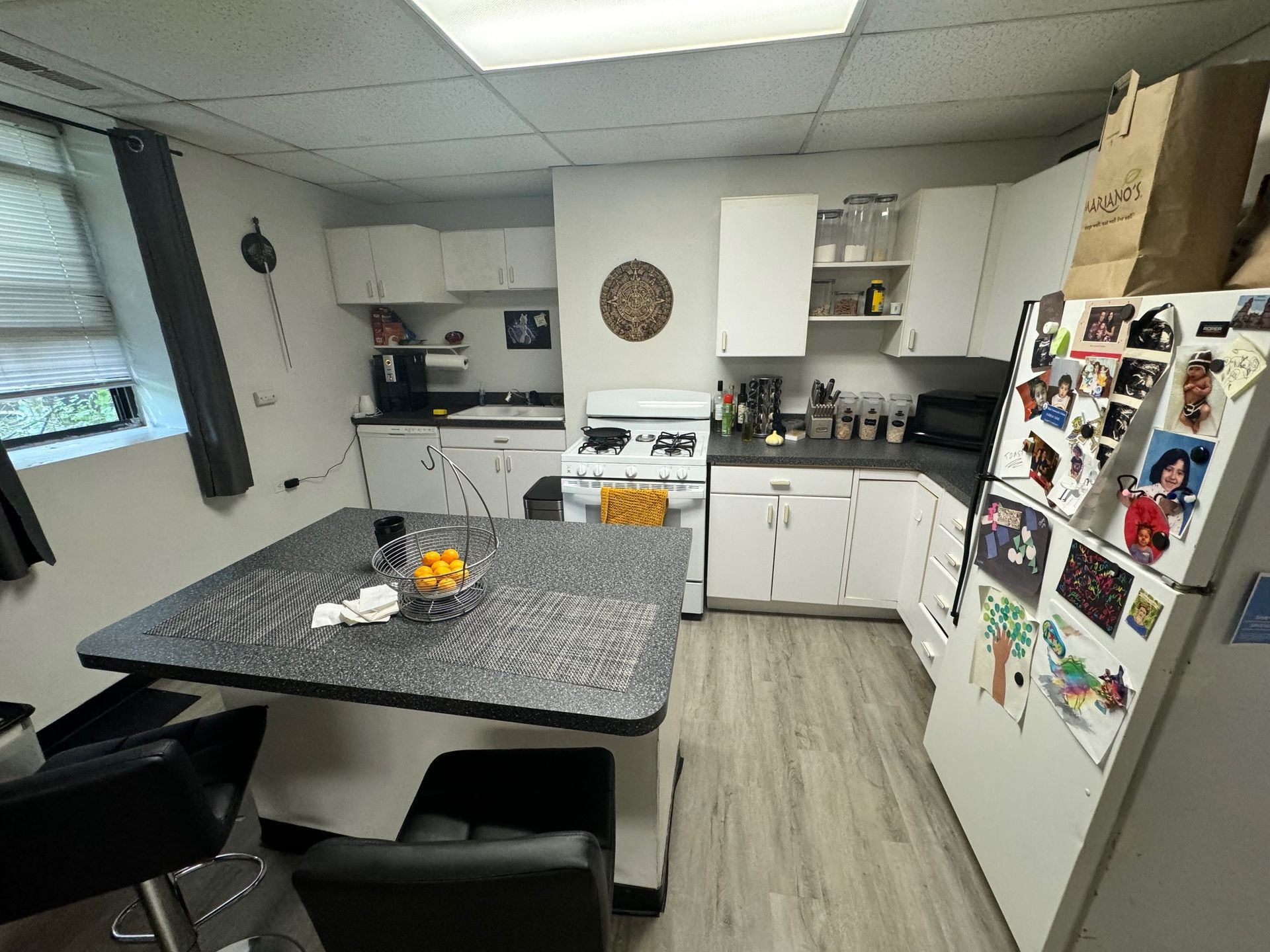 A small kitchen with white cabinets, a central island with bar stools, a gas stove, and a refrigerator covered in magnets.