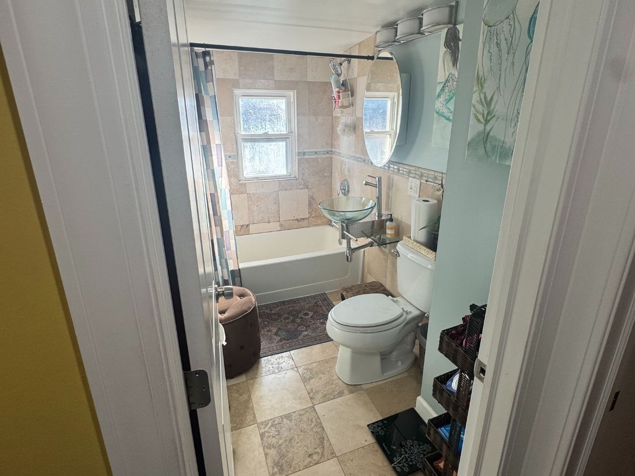 A small bathroom with a bathtub, toilet, and pedestal sink on tiled floors, viewed through a doorway.