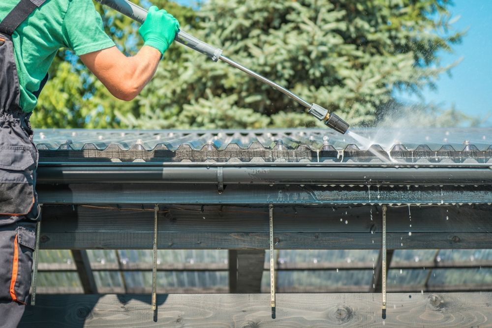 A man is cleaning a gutter with a high pressure washer.