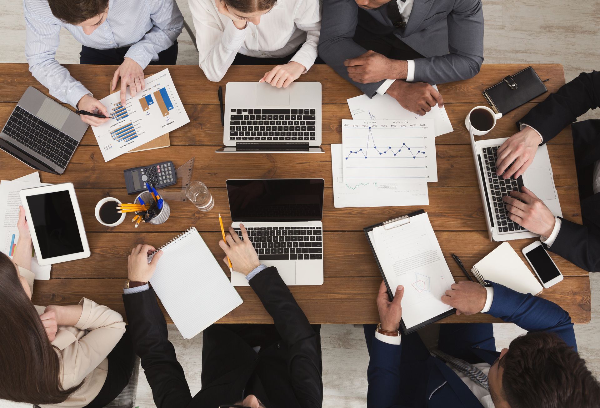 Business team at a wooden table reviewing documents and using laptops.