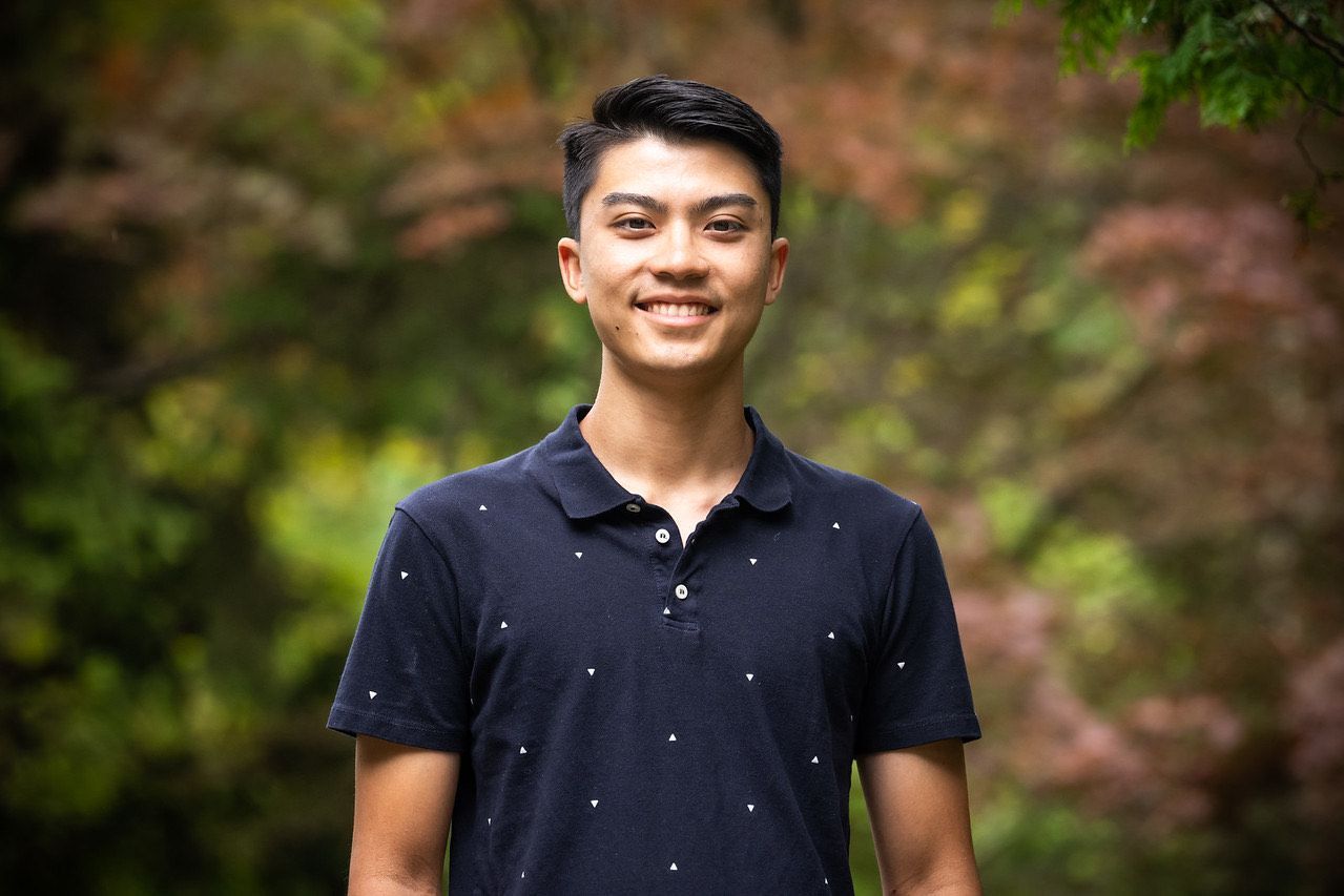A young man in a blue polo shirt is smiling for the camera.