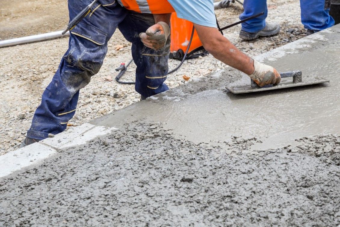 Construction worker smoothing wet concrete with a trowel, wearing work clothes.