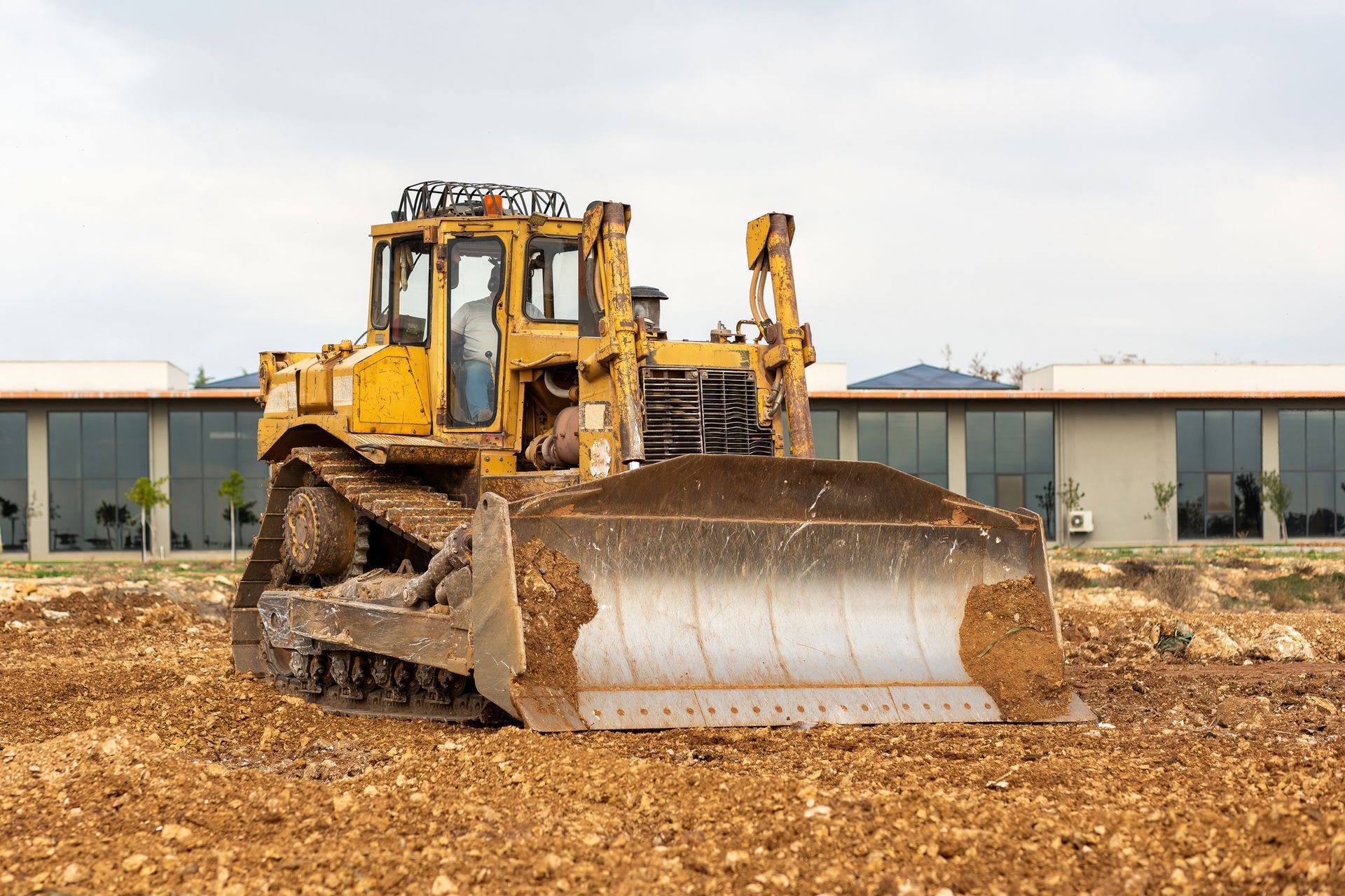 Bulldozer pushing dirt at construction site in front of modern commercial buildings.