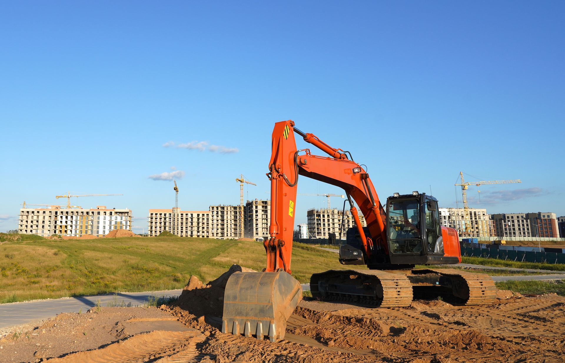 Excavator digging soil at construction site with new buildings and cranes in background.