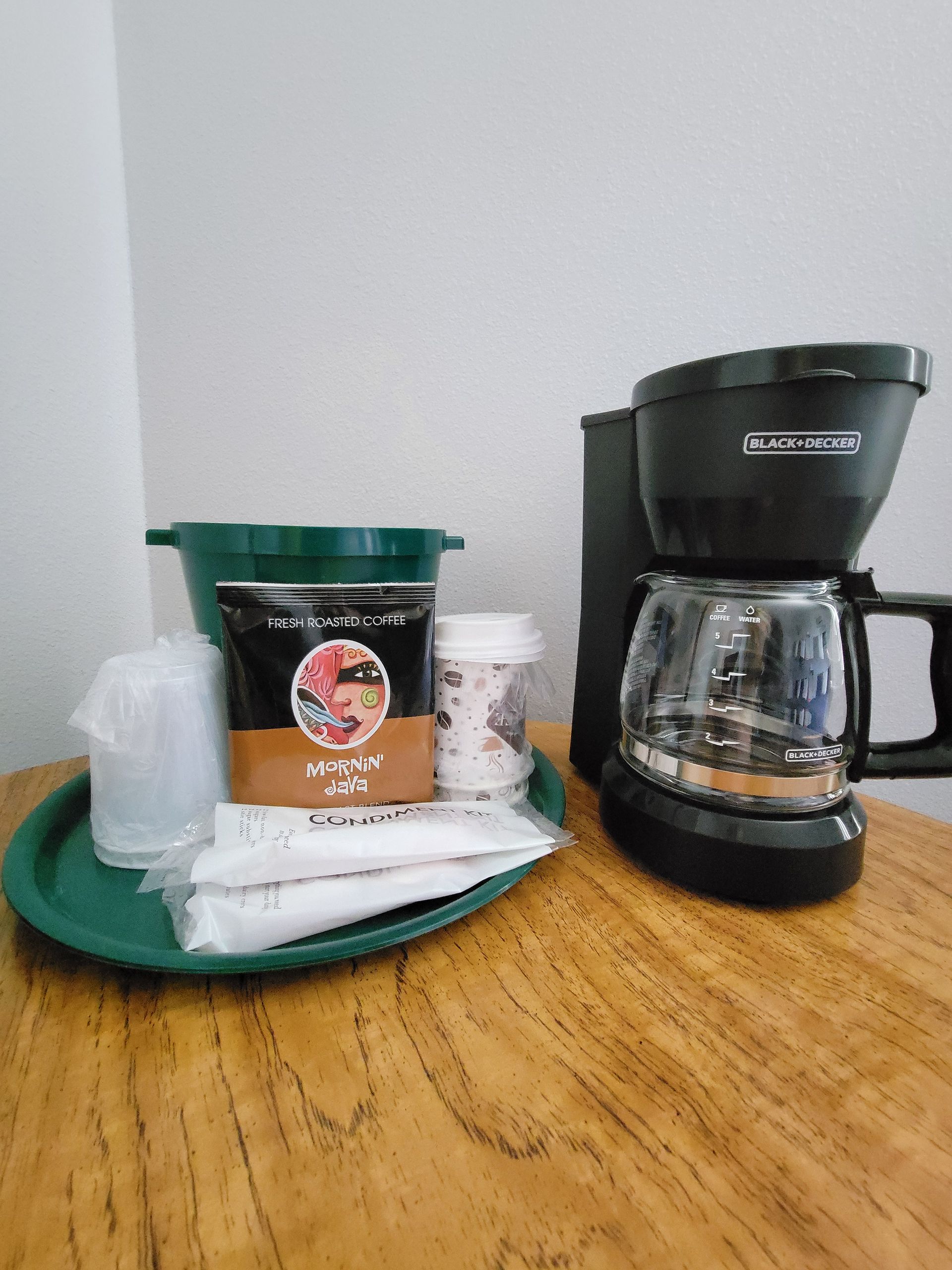 Coffee maker, cups, and supplies on a green tray on a wooden table.