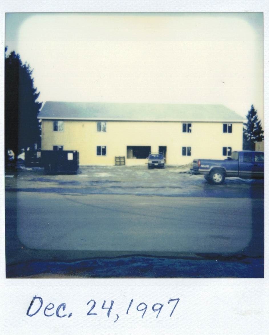 Two-story yellow building on a paved lot. Cars parked outside. Dated Dec. 24, 1997.