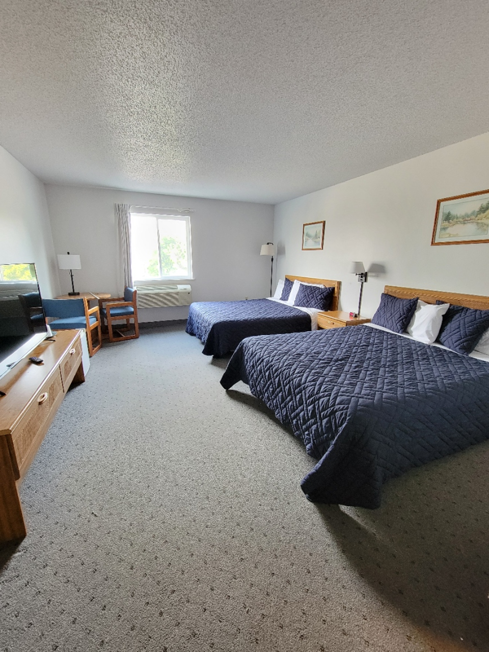 Bedroom with two double beds, nightstands, TV on a wooden stand, and a window.