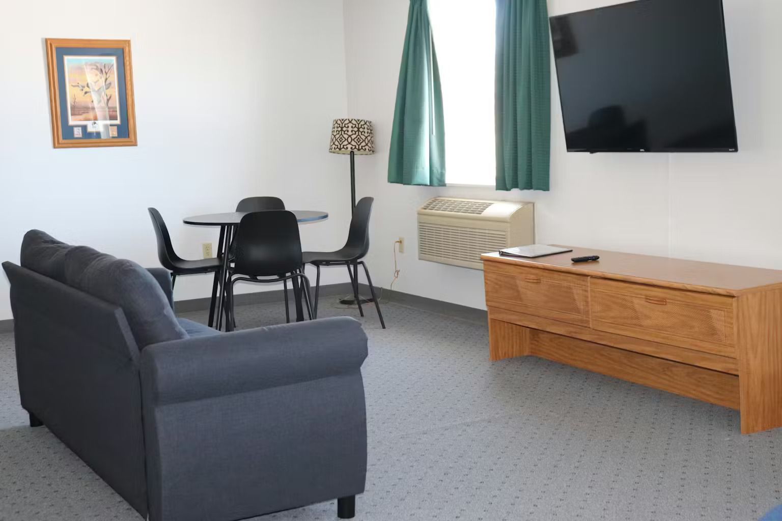 Living area with gray sofa, round table with chairs, TV, and window with green curtains.