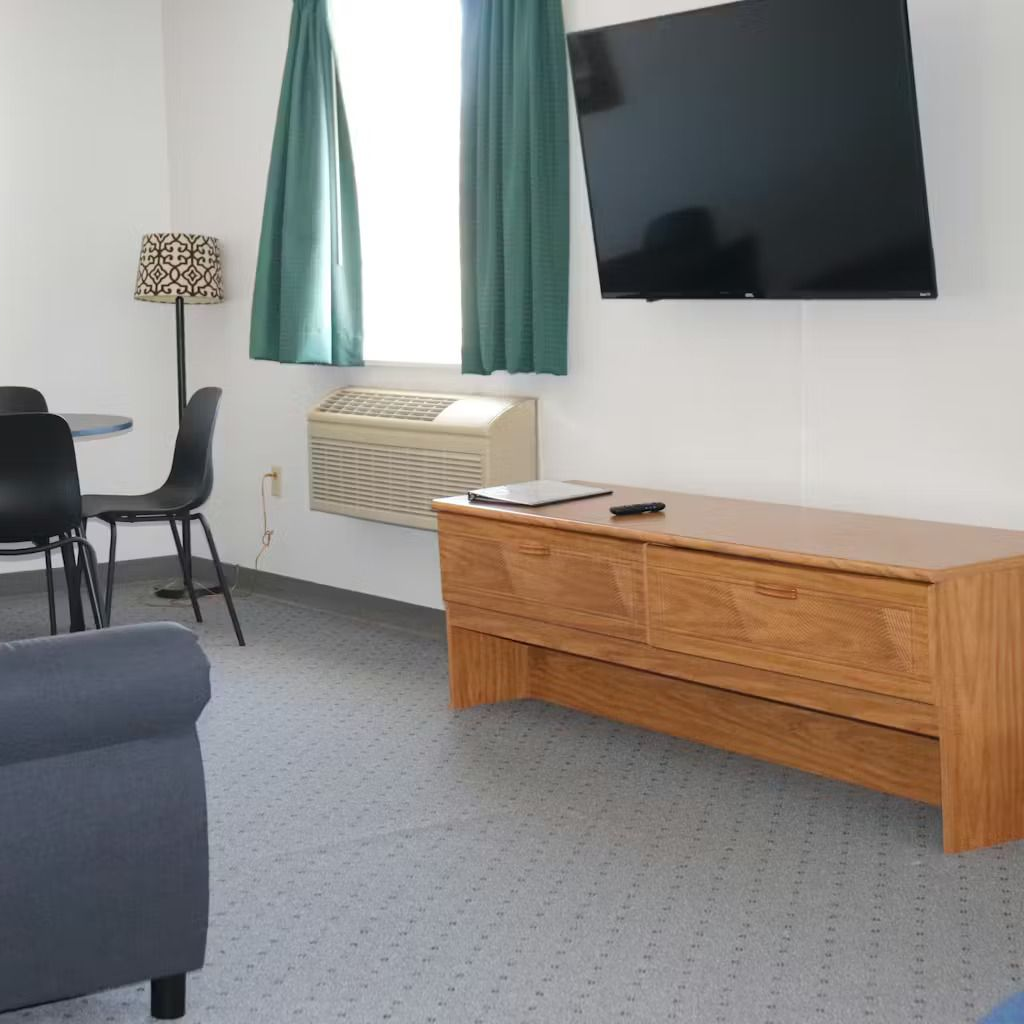 A hotel room with a TV, table, chairs, sofa, and window with teal curtains.