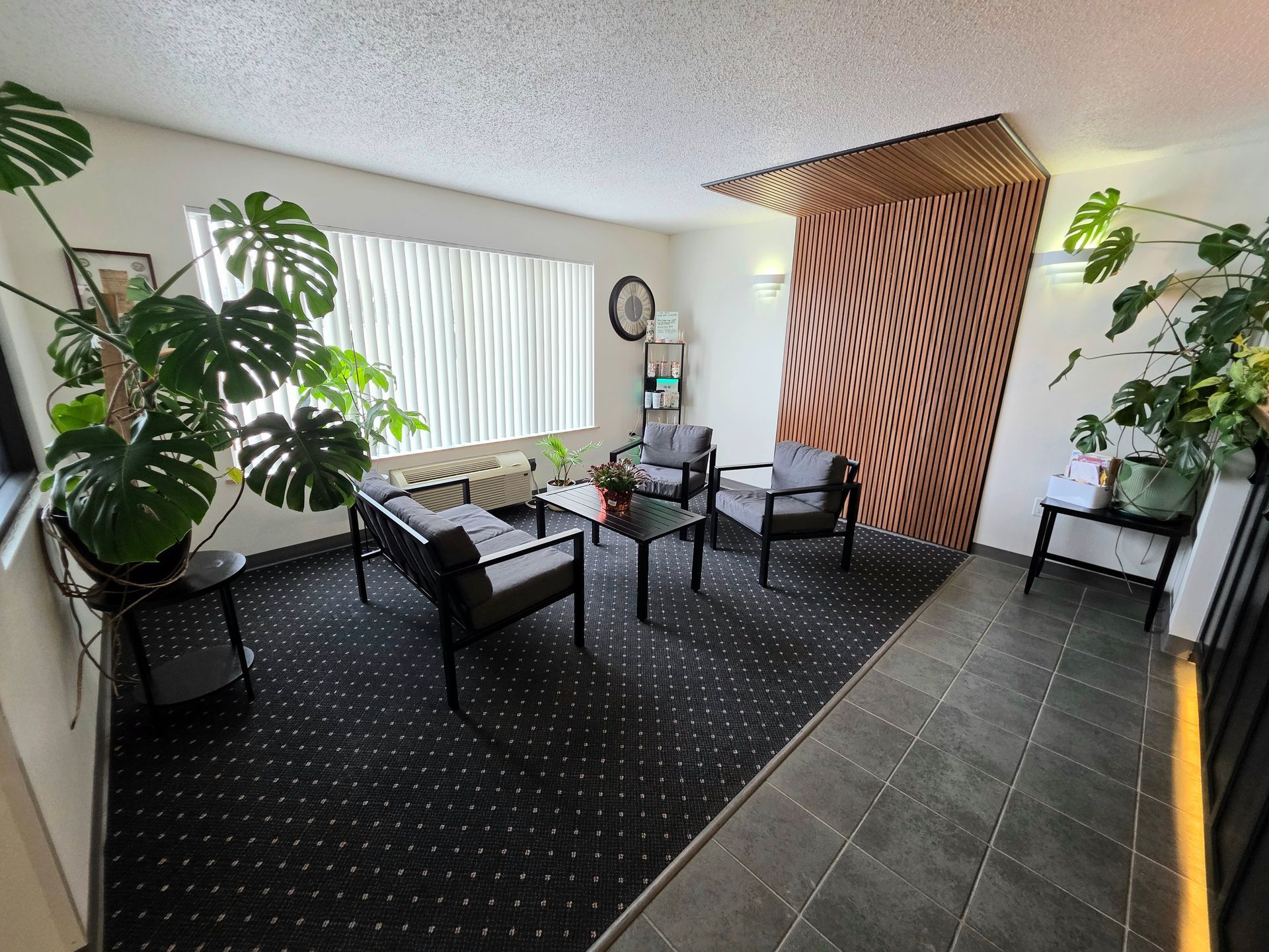 Waiting area with gray chairs, plants, and patterned rug.