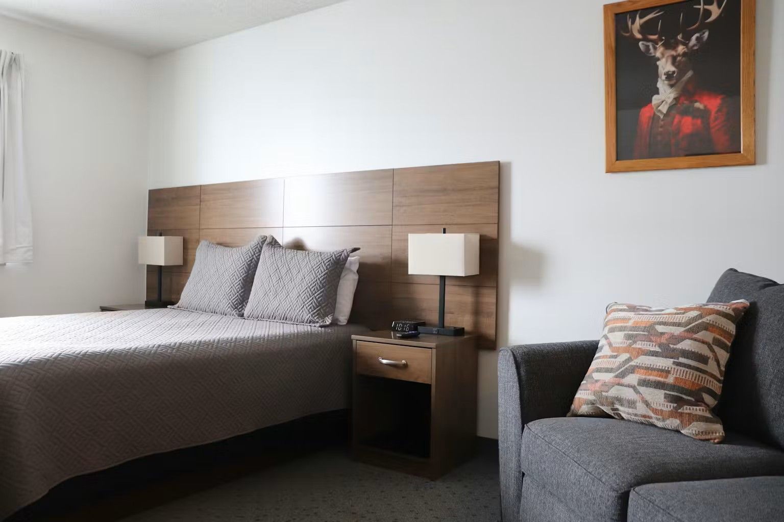 Bedroom with a bed, nightstand, sofa, and framed art. Neutral colors, modern design.