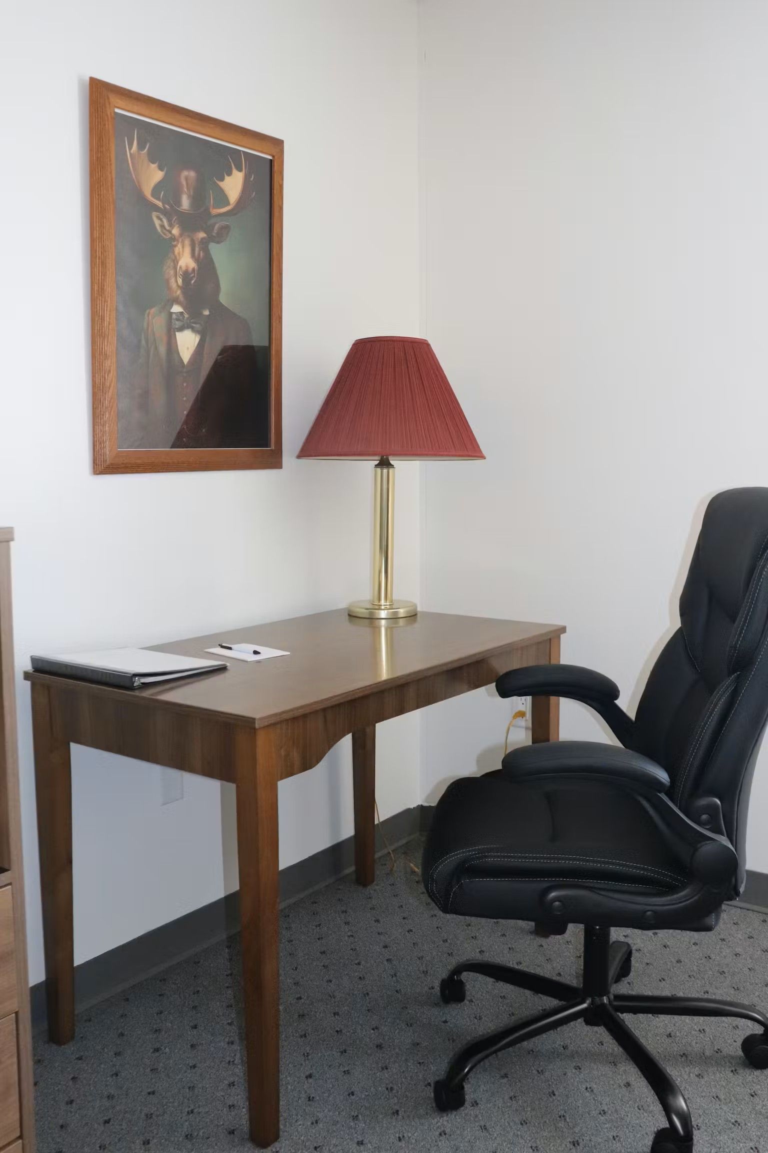 Office desk with lamp, chair, and framed artwork of a deer in a suit.
