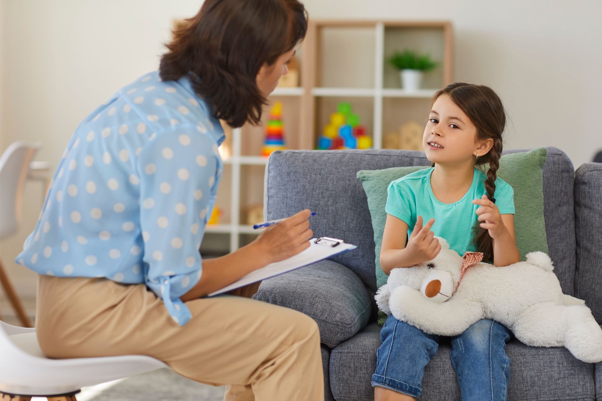 Woman interviewing child sitting on a sofa, child holding teddy bear.