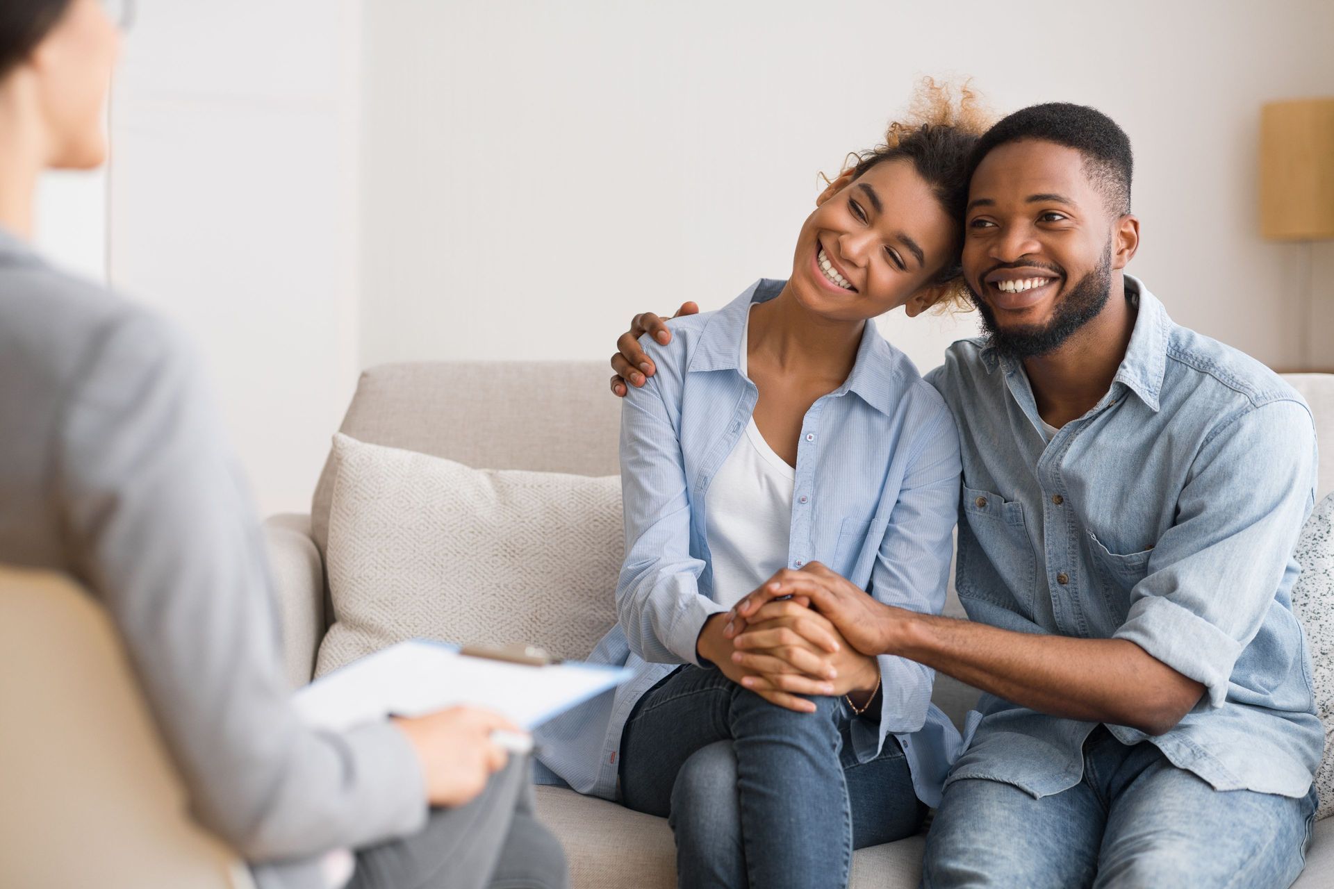 Couple smiling, holding hands, sitting on a sofa during couples therapy session.