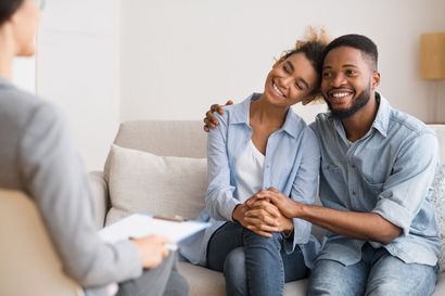 Couple smiling, holding hands, sitting on a sofa during couples therapy session.
