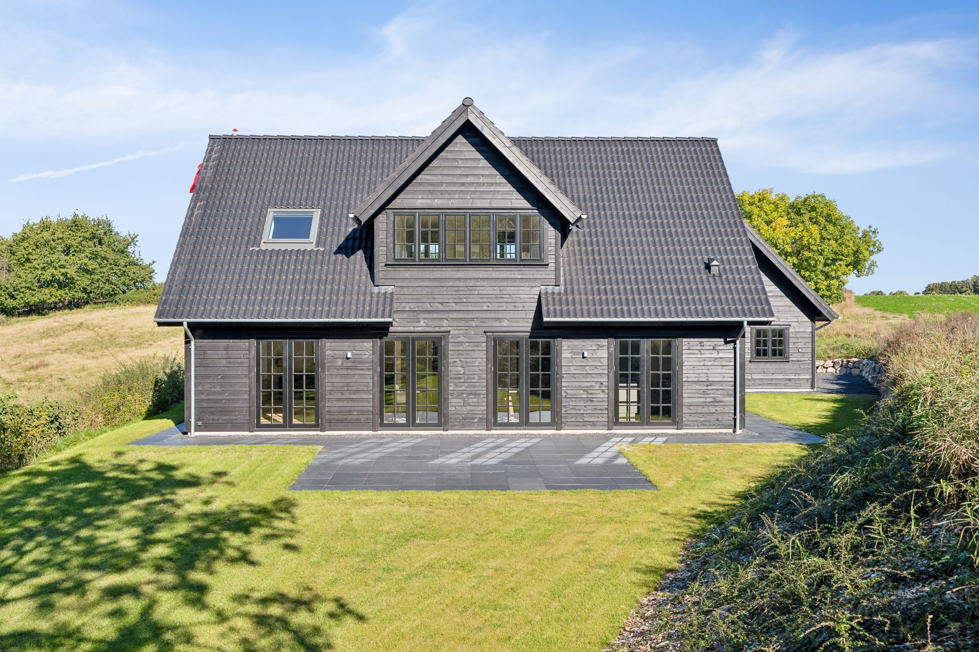 et stort hvidt hus med gråt tag står midt på en græsmark.