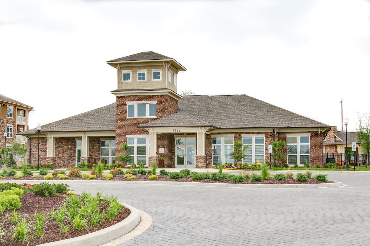Exterior view of a brick clubhouse with glass doors and landscaped front, curved driveway.