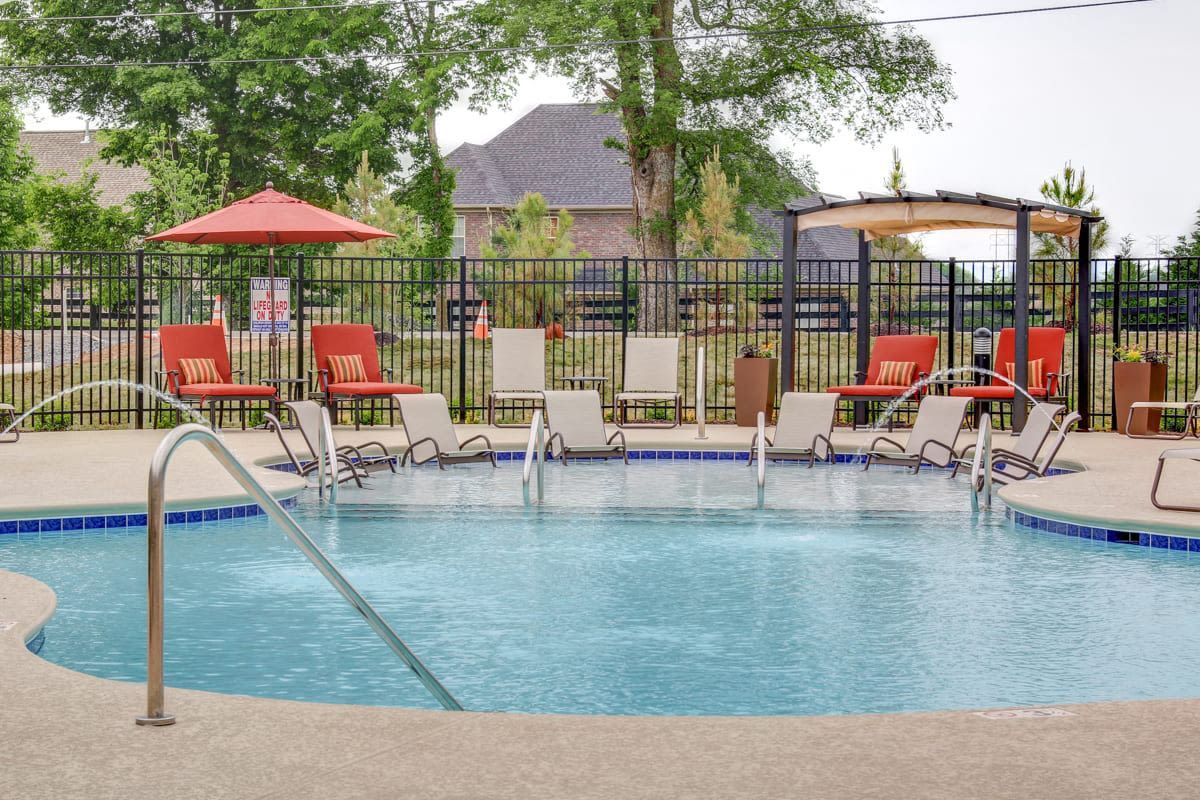 Outdoor pool area at an apartment community with lounge chairs, red umbrellas, and a black metal fence.