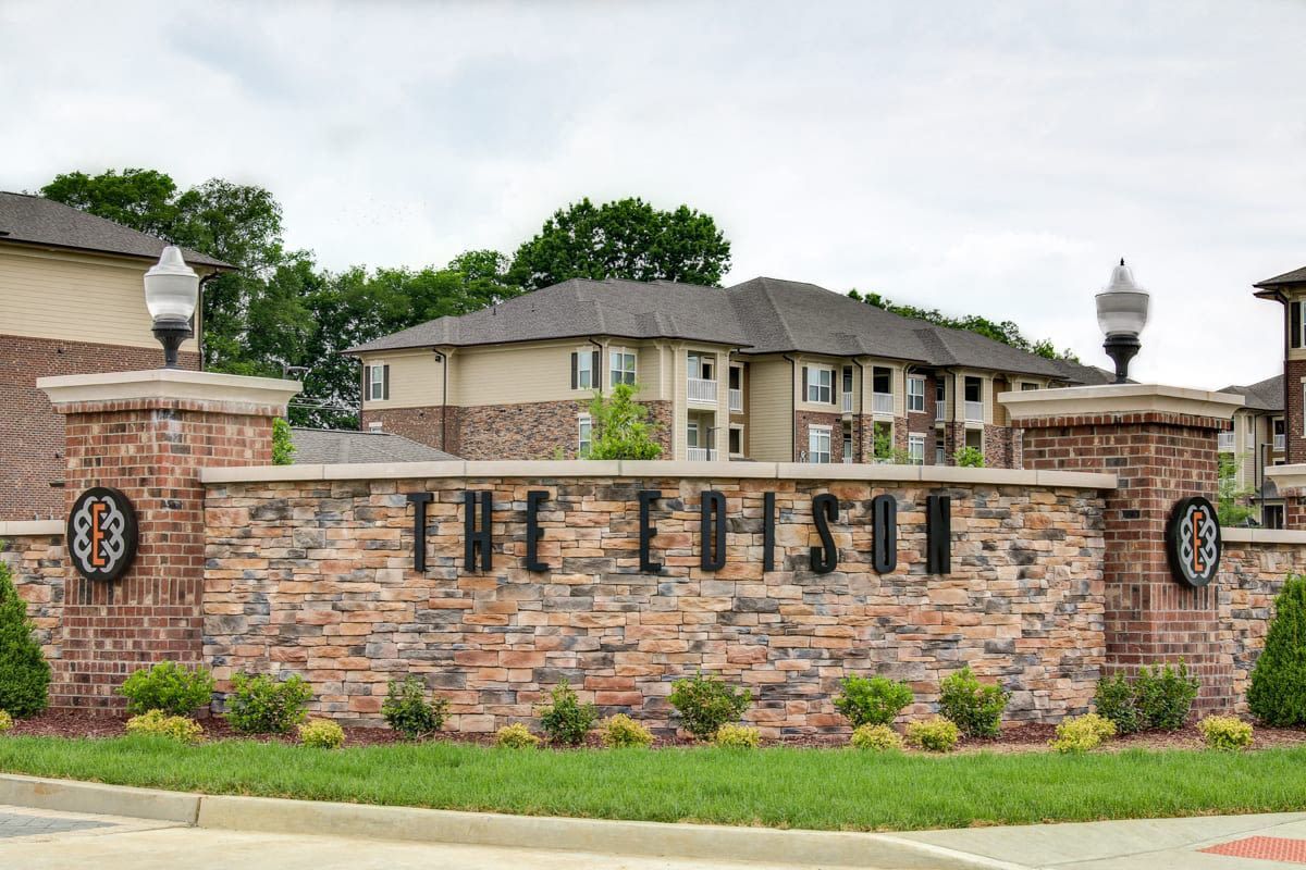 Stone entrance monument with brick pillars and shrubs at an apartment community.