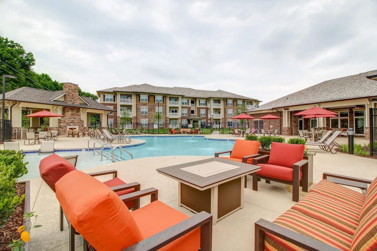 Outdoor pool deck with orange lounge chairs and umbrellas at a residential complex.
