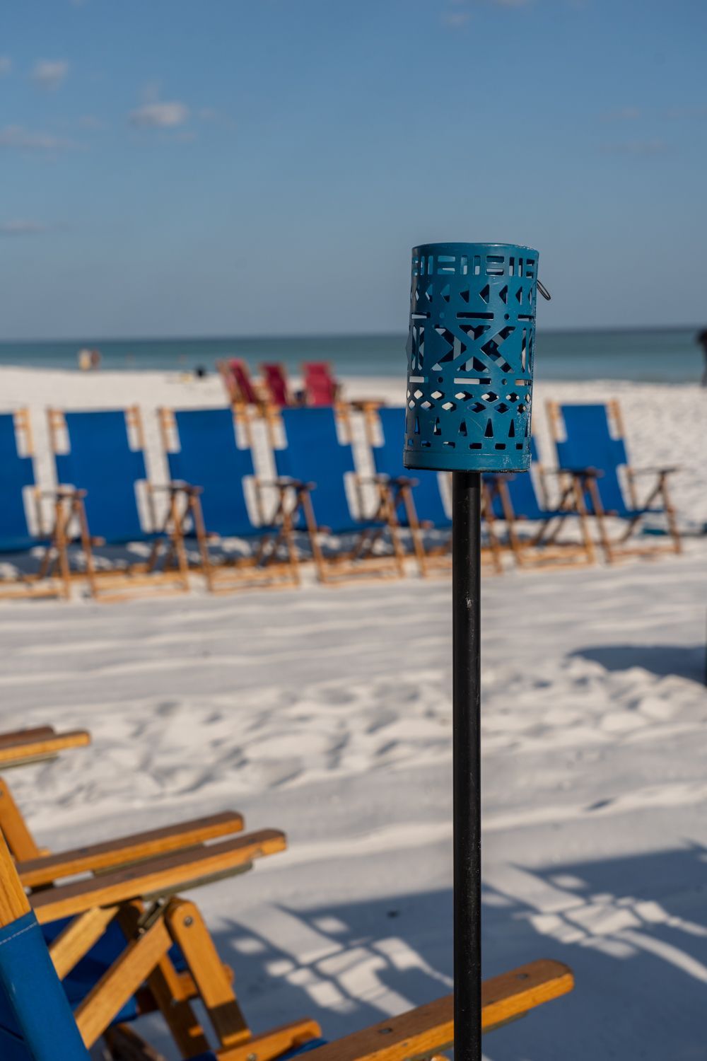 Blue lantern on pole at beach with blue and yellow chairs, white sand, and ocean.