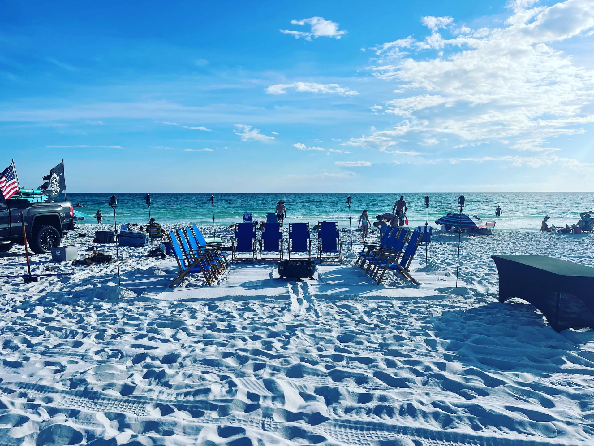 Beach scene with chairs, trucks, and people enjoying a sunny day.